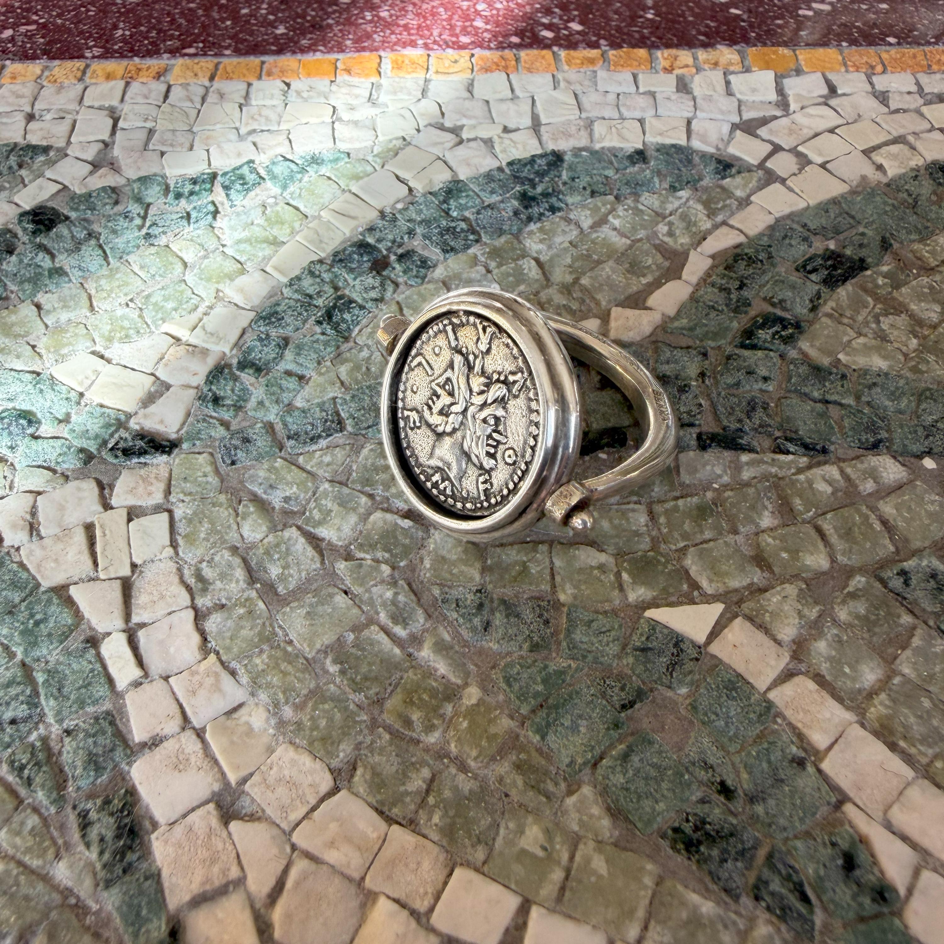 Cette bague en argent sterling met en valeur une authentique pièce de monnaie romaine du IIe siècle A.I.C., à l'effigie du dieu Janus à deux visages. Le revers de la pièce représente Rome debout, érigeant un trophée. L'anneau est rotatif, ce qui