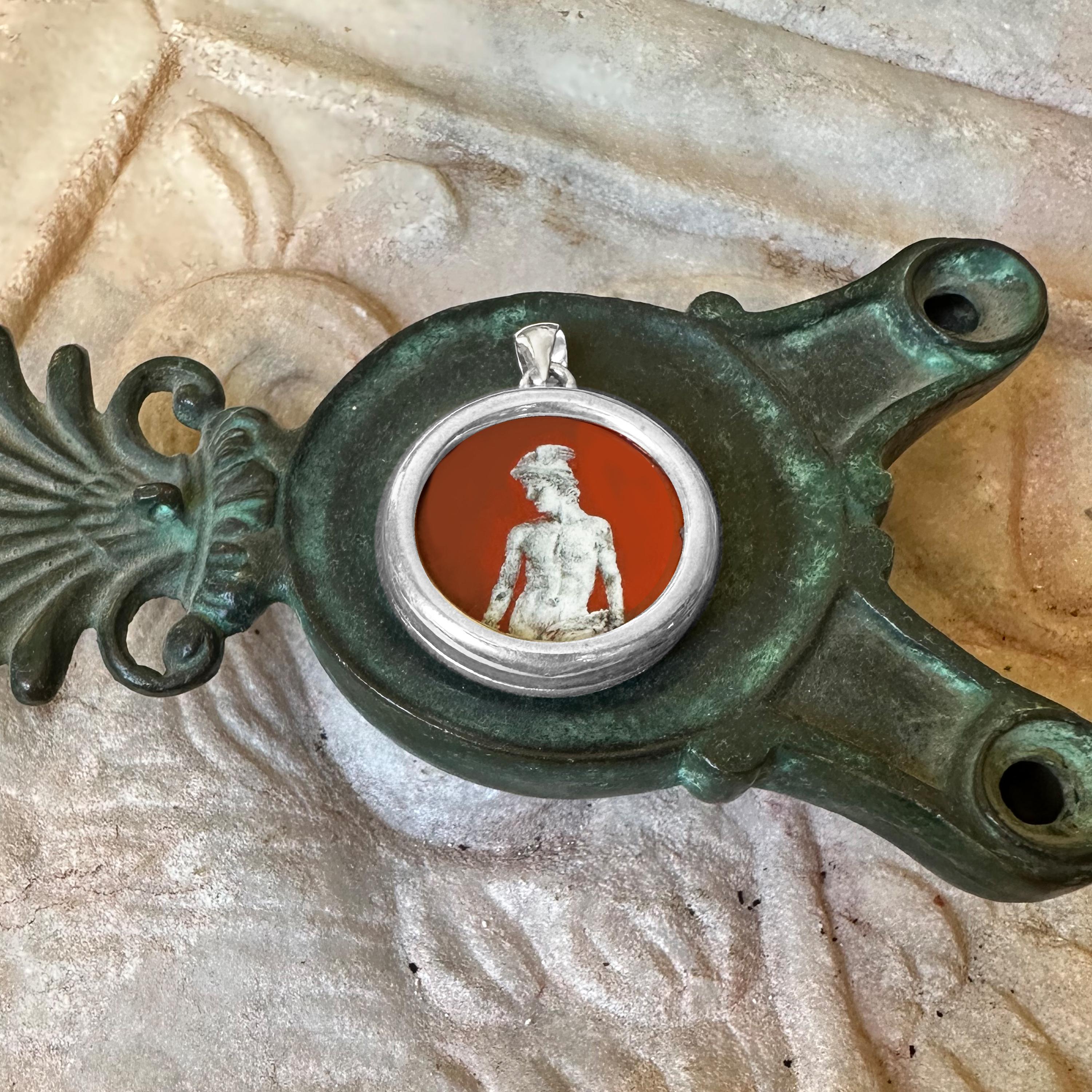 Questo ciondolo presenta un'immagine del dio romano Mercurio dipinta a mano dall'artista Tommaso Rossi su diaspro egiziano. Incastonato in una montatura in argento 925, il design mette in evidenza l'iconico elmo alato e il caduceo di Mercurio,