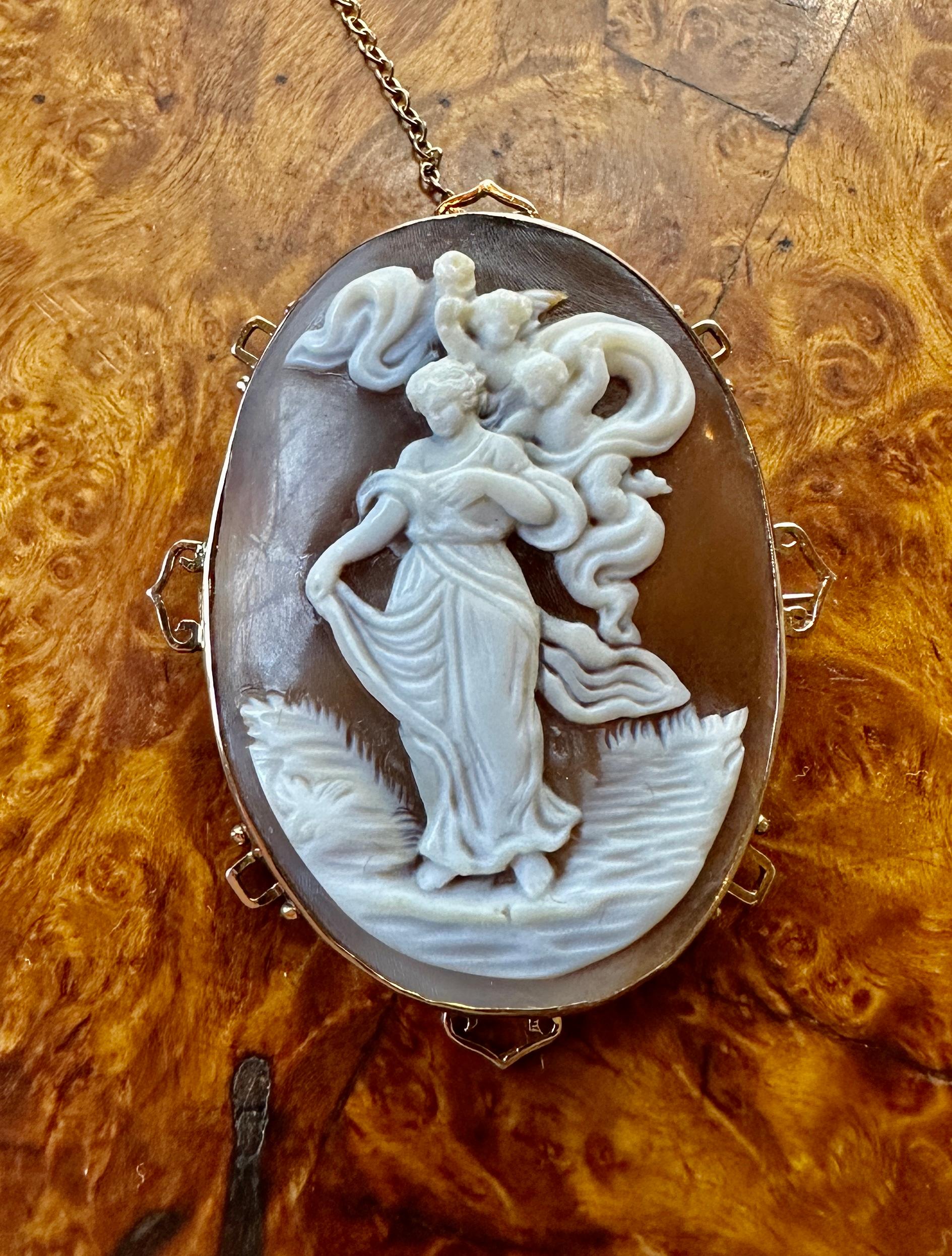 This is an absolutely stunning museum quality antique Victorian Shell Cameo Pendant Brooch in Gold with a hand carved image of a Goddess Maiden with two attendant Cherub, Angel or Putti in the sky. This may be a rendering of Cupid and Psyche. 
The