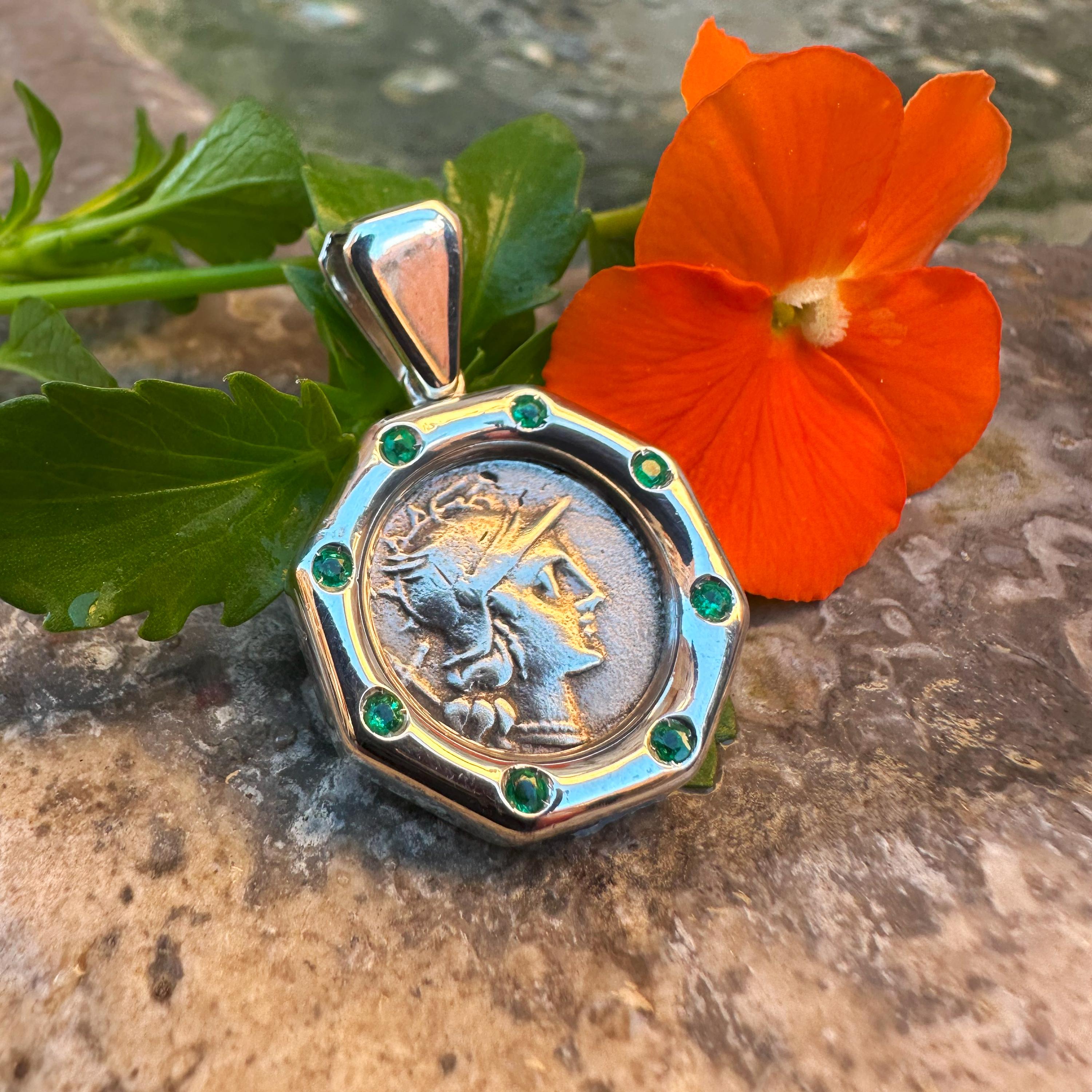 Découvrez un remarquable pendentif en argent orné d'une pièce de monnaie romaine originale en argent datant de 148 av. Cette pièce exquise présente une représentation captivante de la déesse Revere, sertie en argent avec 8 émeraudes 0,6KT. Au revers