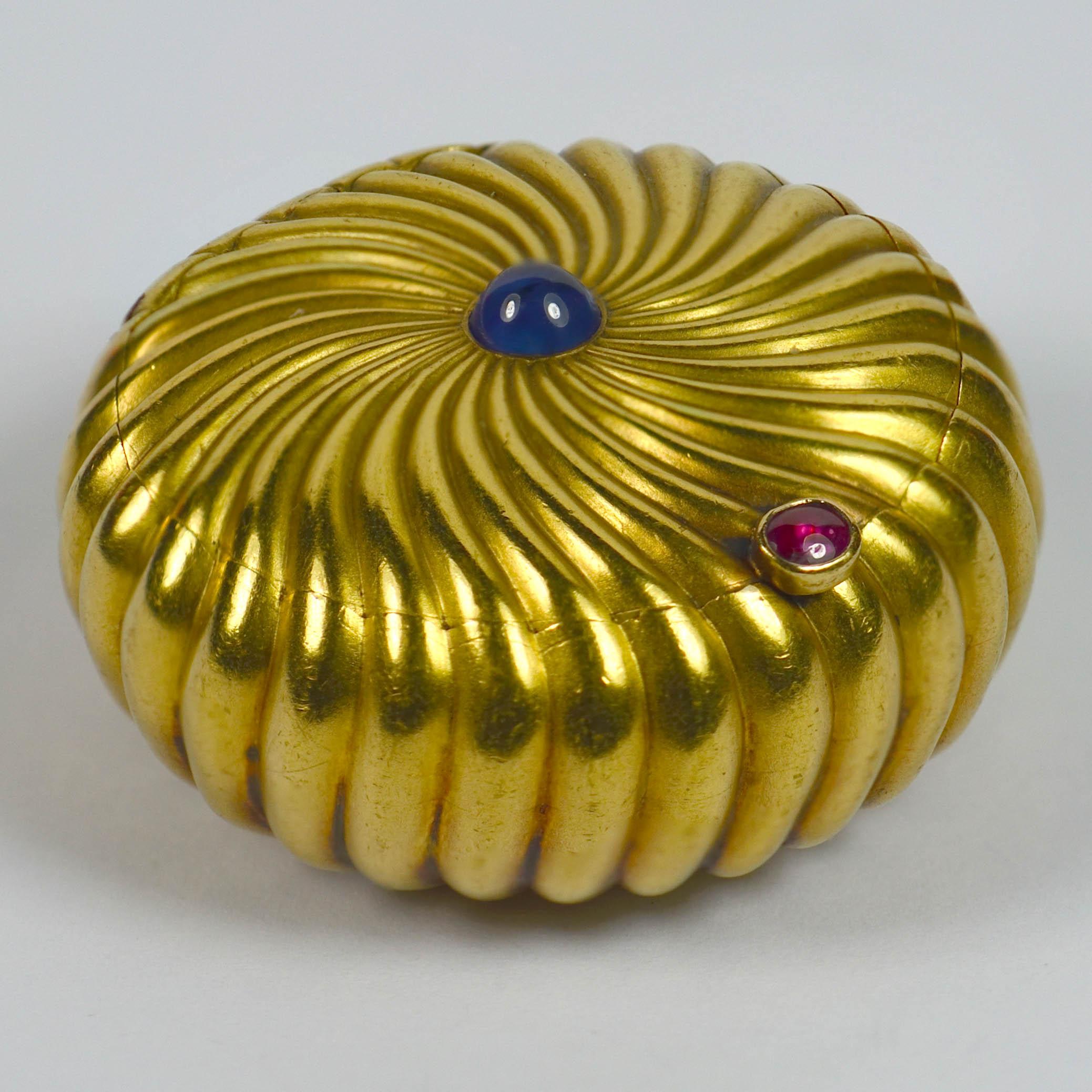 A lovely 18 carat gold pill box with a spiralling godronne motif set with a natural sapphire cabochon to the centre. The opening of the lid is set with a natural ruby cabochon.

Formerly owned by the Duchesse du Massa of France.

French import marks
