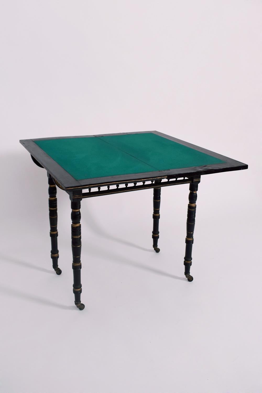 Folding table in blackened wood and gilded wood resting on four turned wooden legs ending in casters. In the style of Godwin. England, late 19th c. 