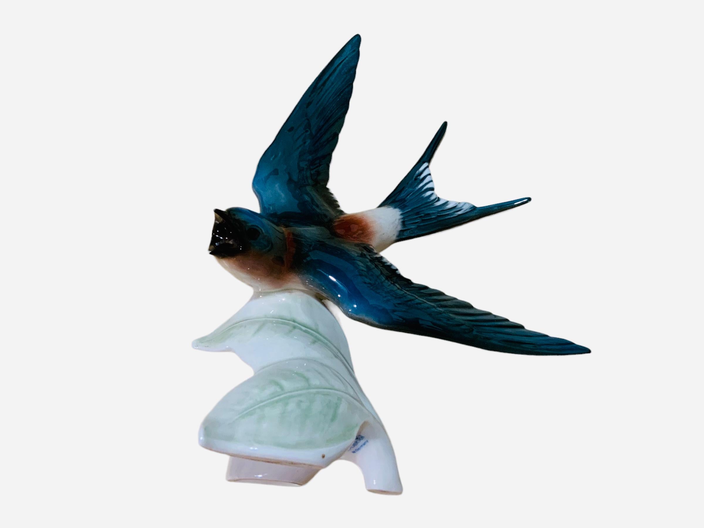 This is a Goebel porcelain figurine of a bird. It depicts a very well done hand painted Red Rumped Swallow. The bird is standing up over a branch with few leaves. It is hallmarked Goebel, W.Germany at the base.