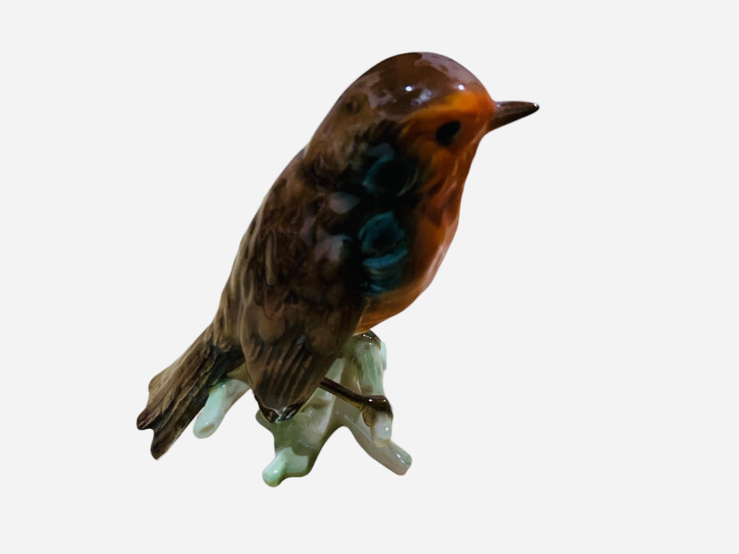 This is a Goebel porcelain figurine of a bird. It depicts a very well done hand painted extreme agile Red-Rumped Swallow. It is standing up over a branch of a tree. It is hallmarked Goebel, W.Germany below the asymmetrical light green base.