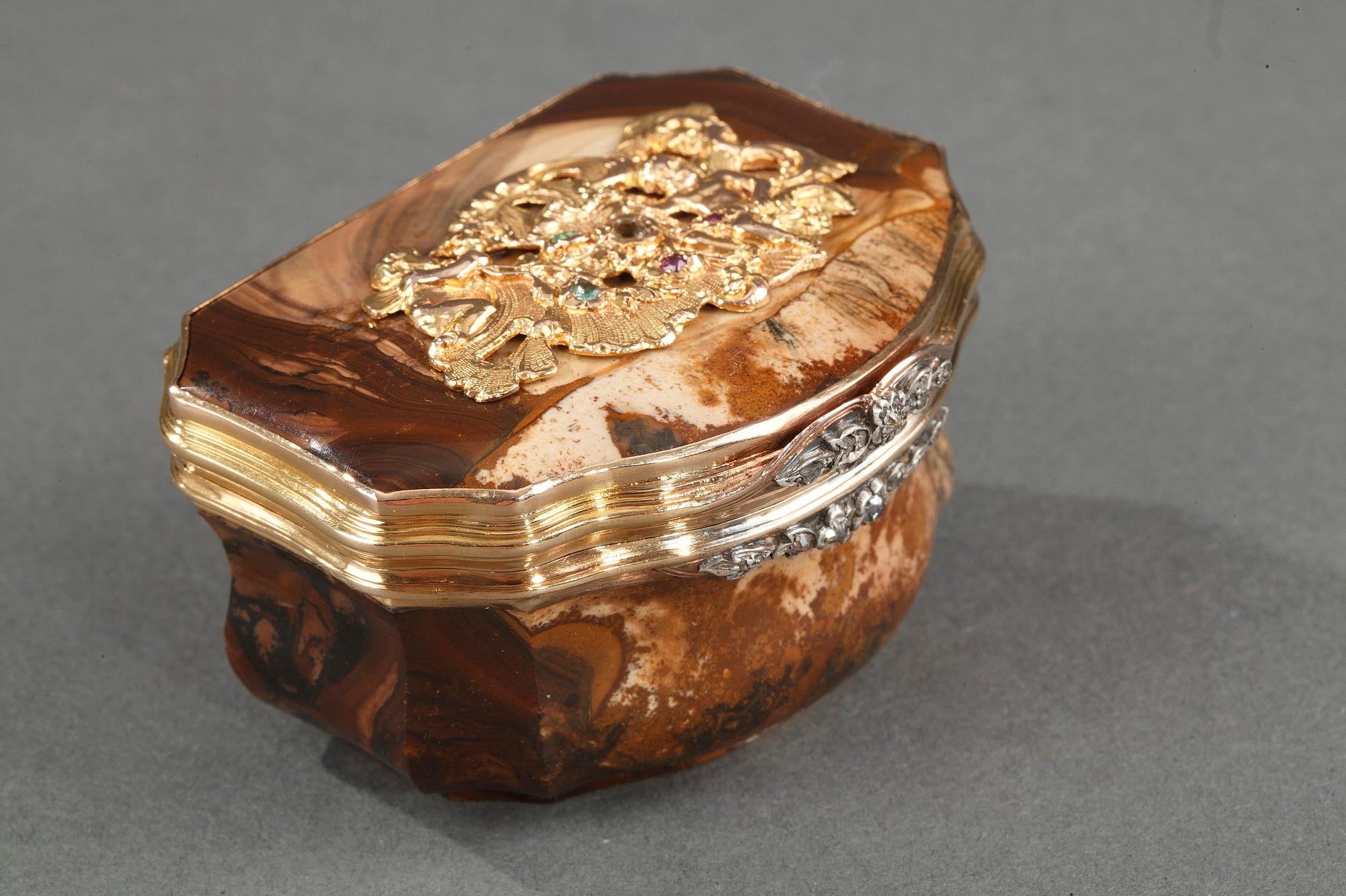 Agate snuffbox with gadrooned body and sculpted gold mountings. The sculpting of the brown agate is enriched by the nuances of the veins in the stone. The center of the hinged lid is decorated with an asymmetrical, openwork Rocaille motif. This