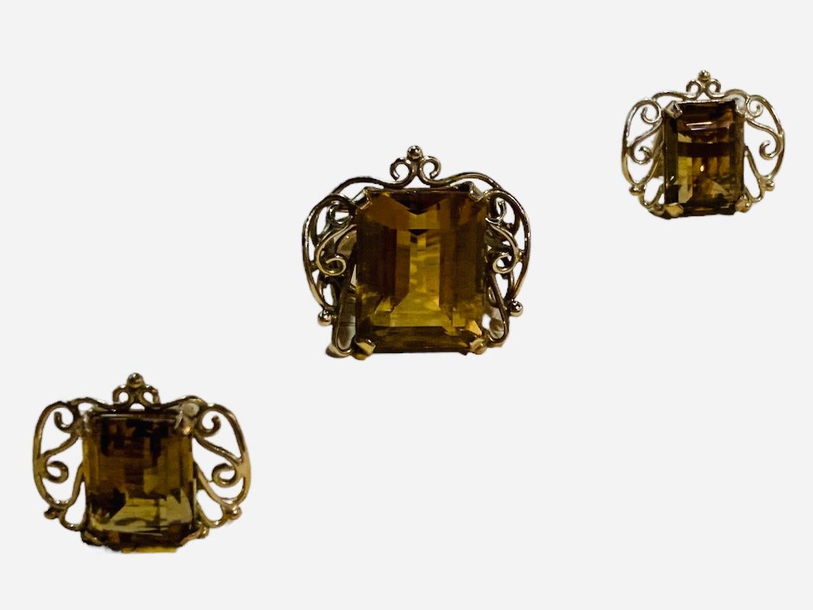 This is a Gold Amber Color Stone Demi Parure. It depicts a yellow gold set of a pair of earrings and a ring containing an emerald cut yellow stones in prong setting and their borders are adorned with scrolls. They are mounted in yellow gold. The