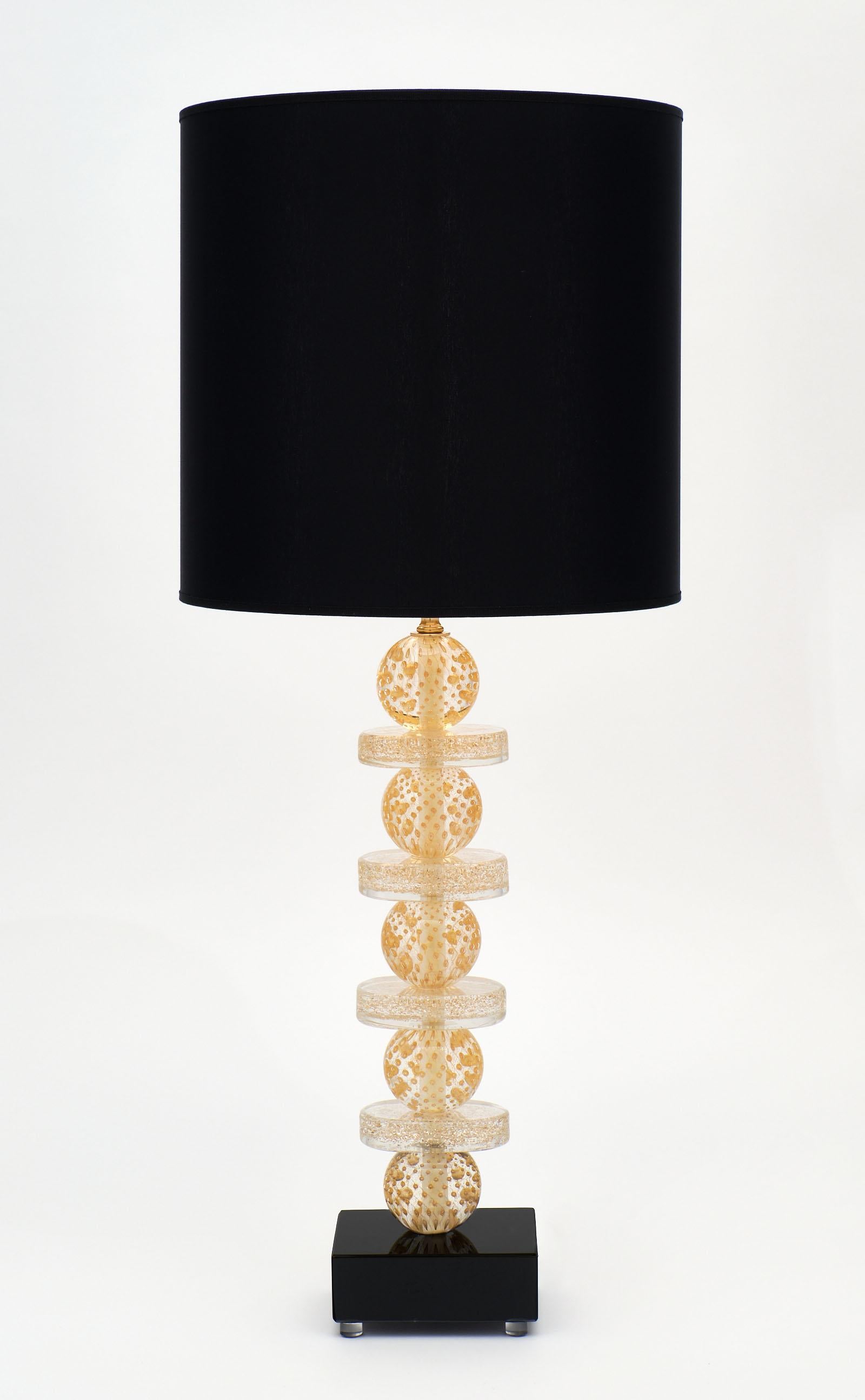 A pair of Murano glass gold and black lamps featuring a combination of glass spheres and rings in the Avventurina technique, created by infusing the glass with 23 carat gold leaf. The stem rests on a black glass base, and the height of glass is