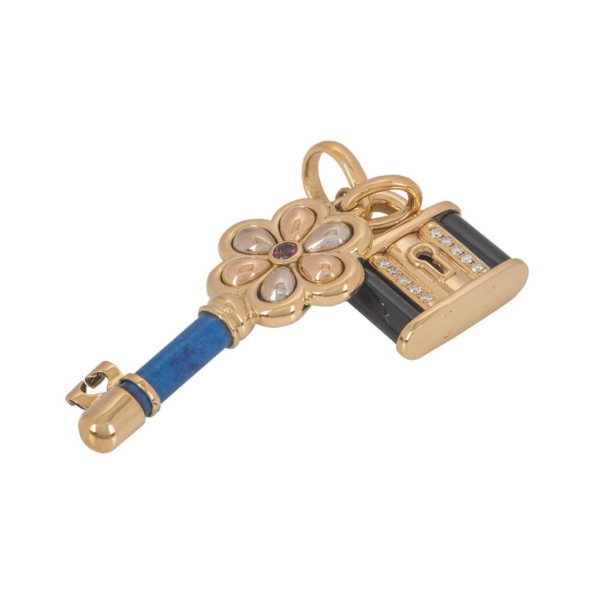 An 18k yellow floral gold key and lock pendant. The key features a flower design head with a single pink tourmaline in the centre and a stem made from lapis. The lock features a key hole with 5 round brilliant cut diamonds beside it and onyx on each