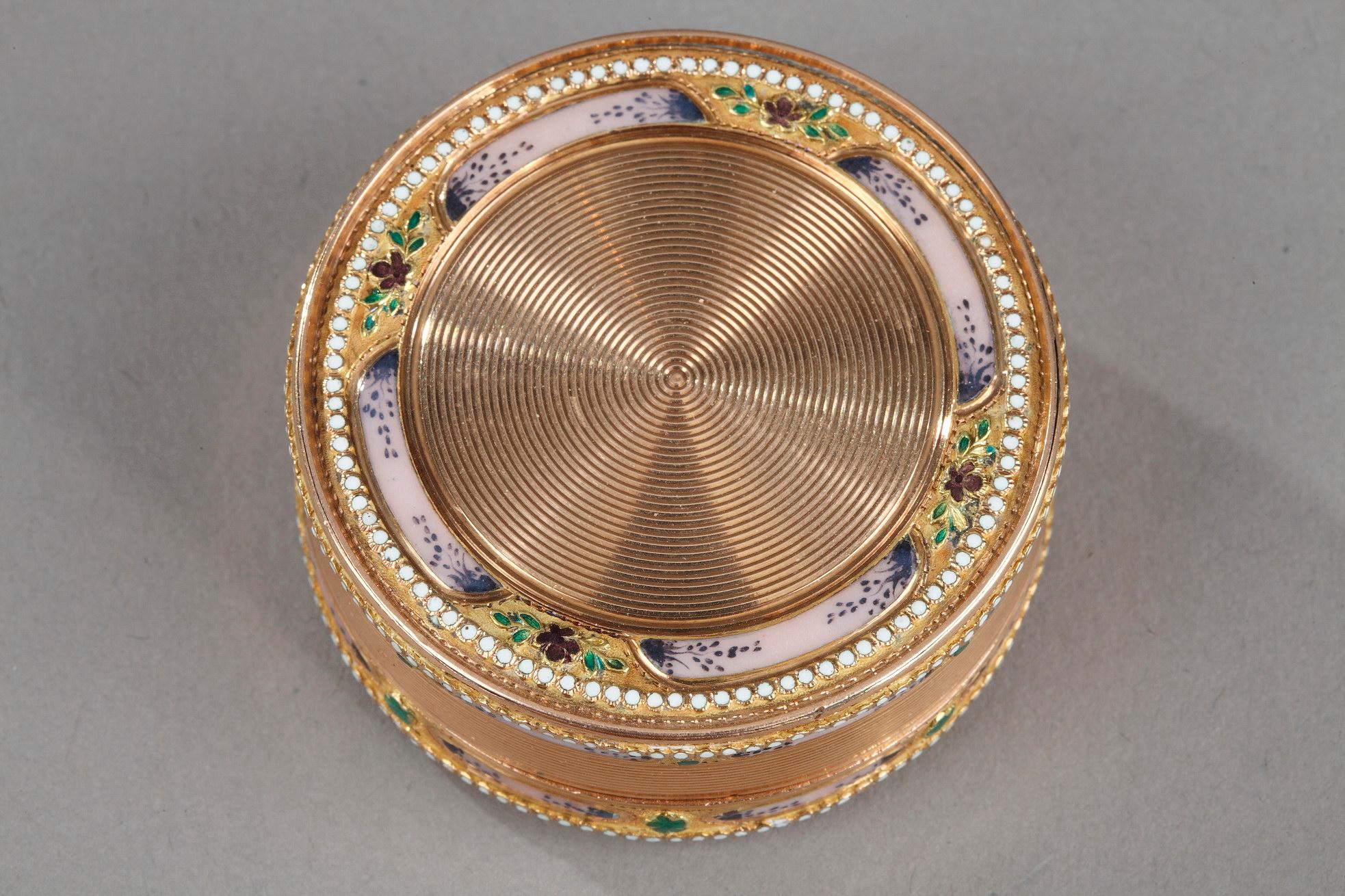 Circular gold and enamelled box. The independent lid decorated with a guilloche in parallel and concentric streaks. This pattern is highlighted by small pink and translucent enamelled panels alternating with green enamel flower patterns. The quality