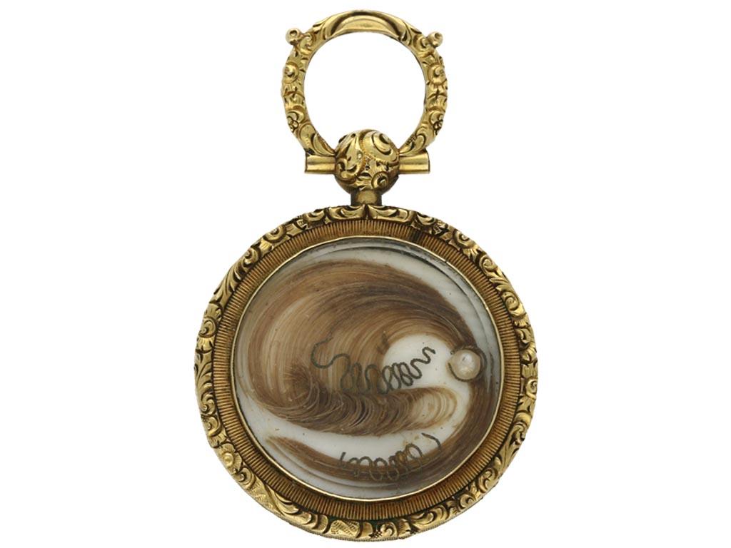 Gold and enamel memorial pendant with locket back. A disk form pendant centrally decorated with a circular enamelled plaque containing a blue forget-me-not flower on a black background, the outer edge of the disk decorated with a black border inset