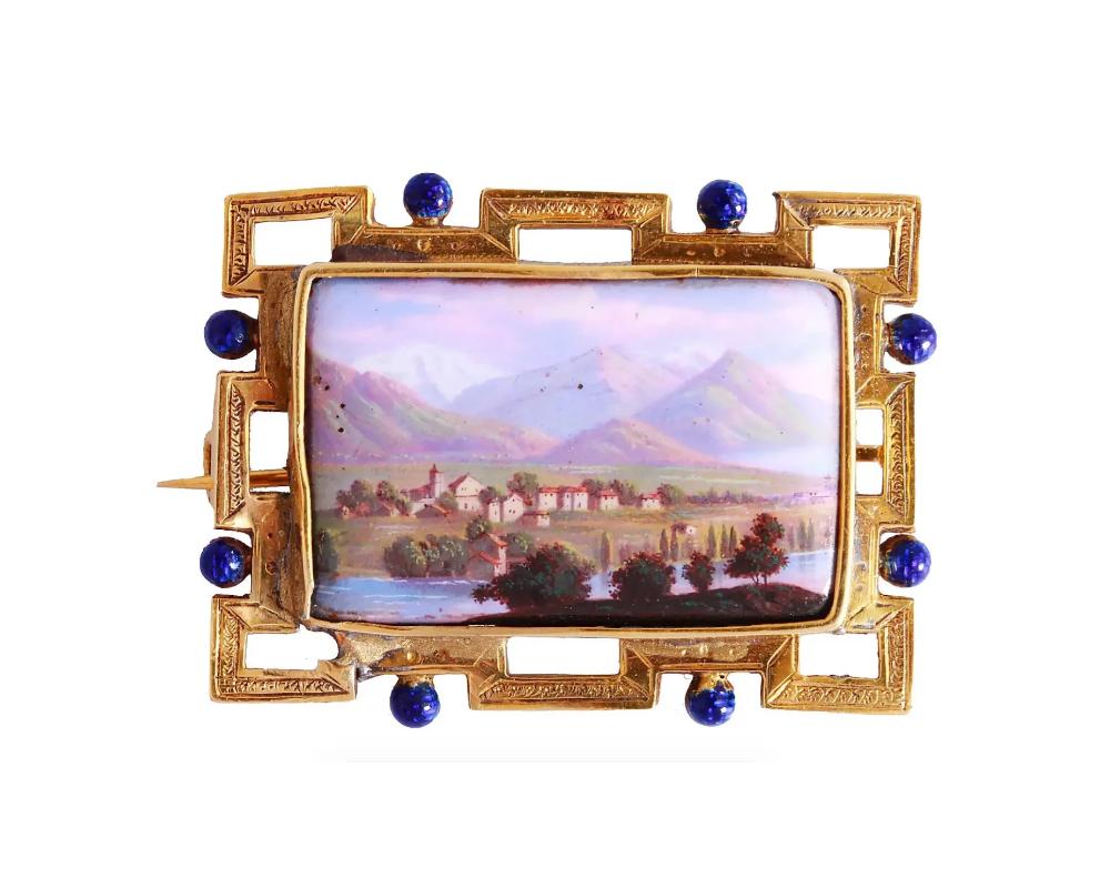An antique late 19th-century pin brooch. A hand-painted enamel miniature represents a Swiss landscape, a village by the lake with mountains in the background. The miniature is enclosed in a geometrical gold frame with engraved and blue enamel