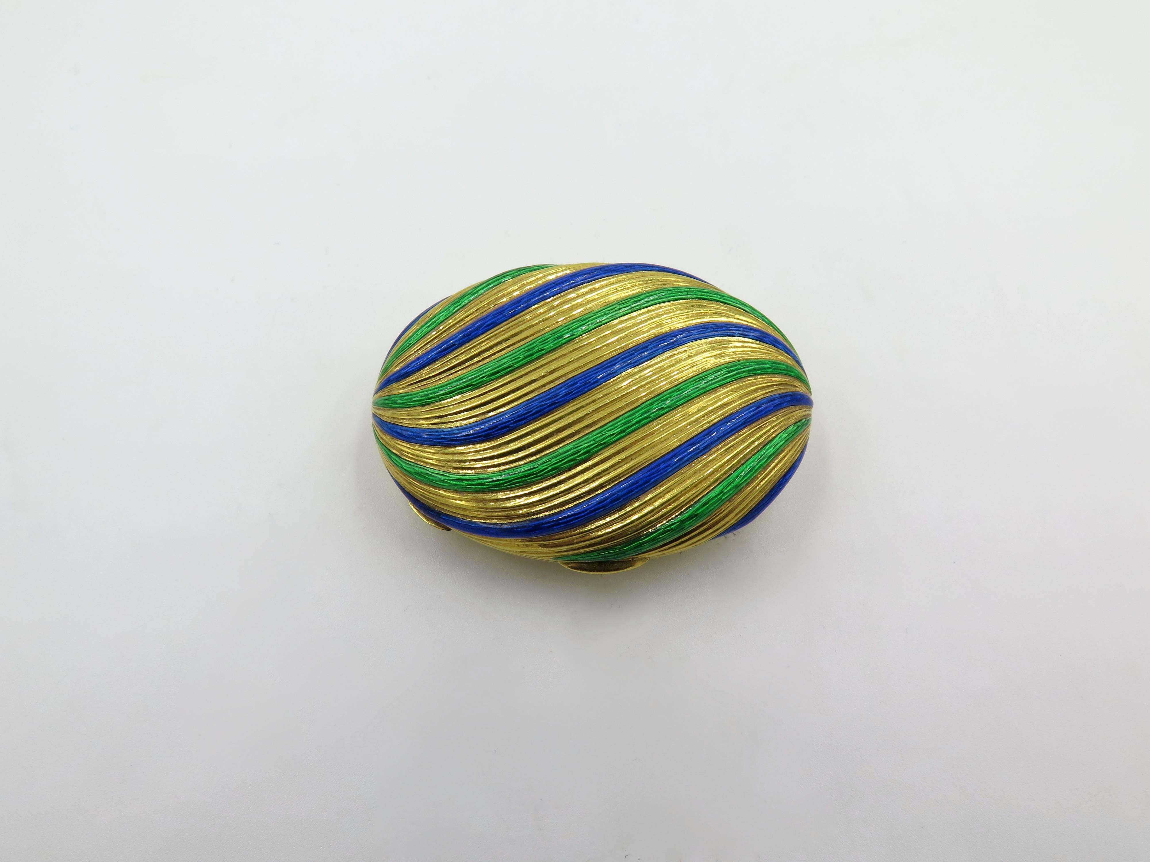An 18 karat yellow gold and enamel pill box. Of oval outline, the top decorated by a fluted pattern, enhanced by blue and green enamel. The box measures approximately 2 x 1 1/2 inches, gross weight is approximately 37.9 grams. 