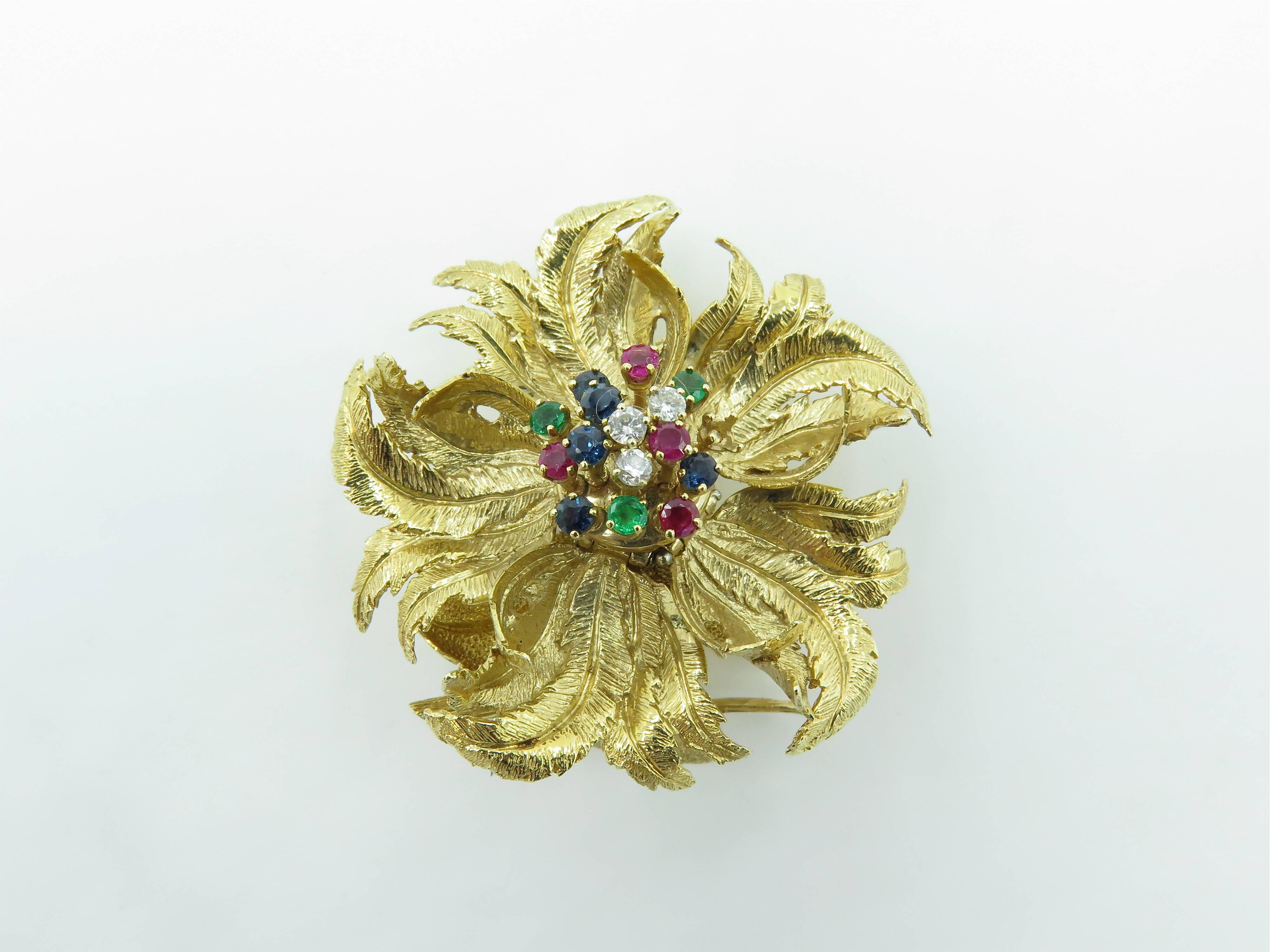 A 14 karat yellow gold, gem set and diamond brooch. Designed as an textured gold flower, with articulated petals, centering a cluster of circular cut diamonds, rubies, emeralds and sapphires. Length is approximately 1 3/4 inches. Gross weight is