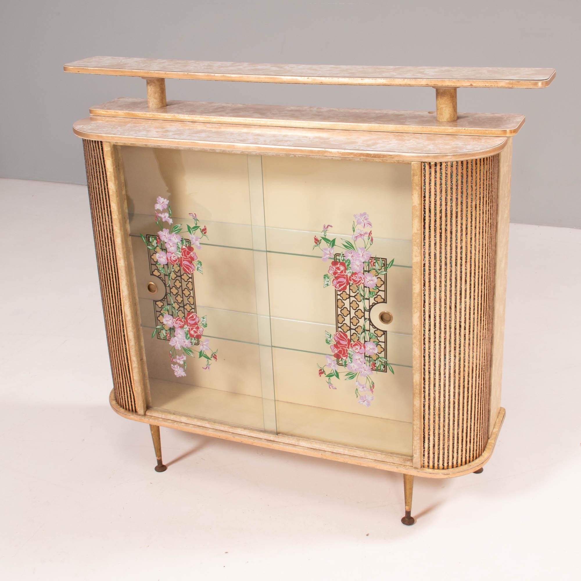 A vintage 1960’s bar unit featuring a marble effect Formica top and a front cabinet for storage. 

Sitting on brass legs, the unit has curved speckled corners with brass detailing.

The cabinet has glass shelves and sliding glass doors,