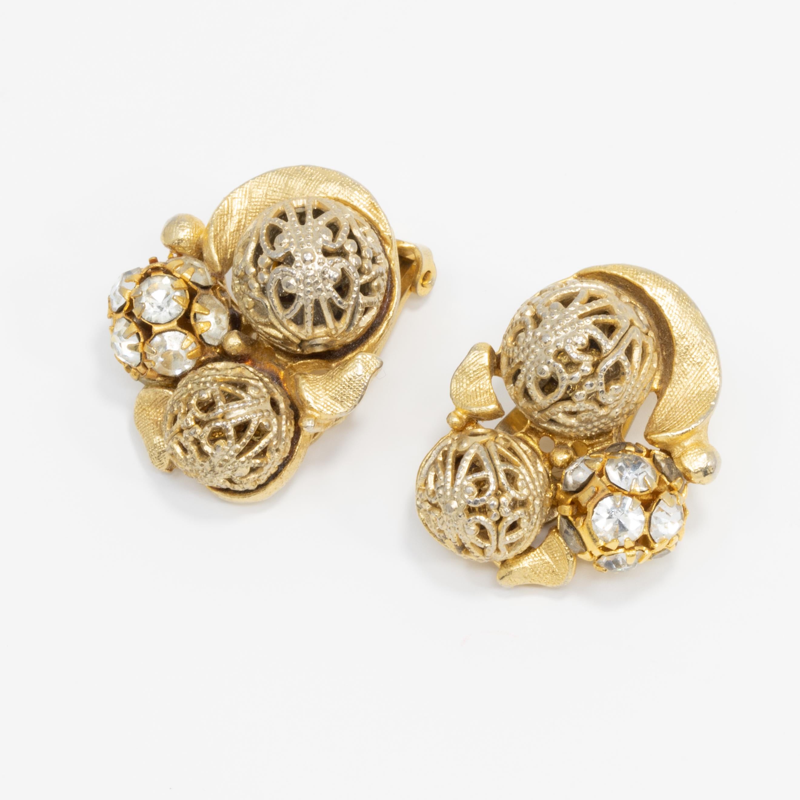 A pair of mid 1900s chunky retro earrings. Each features decorative filigree metal and pave-crystal balls on a gold-plated metal clip on setting.
