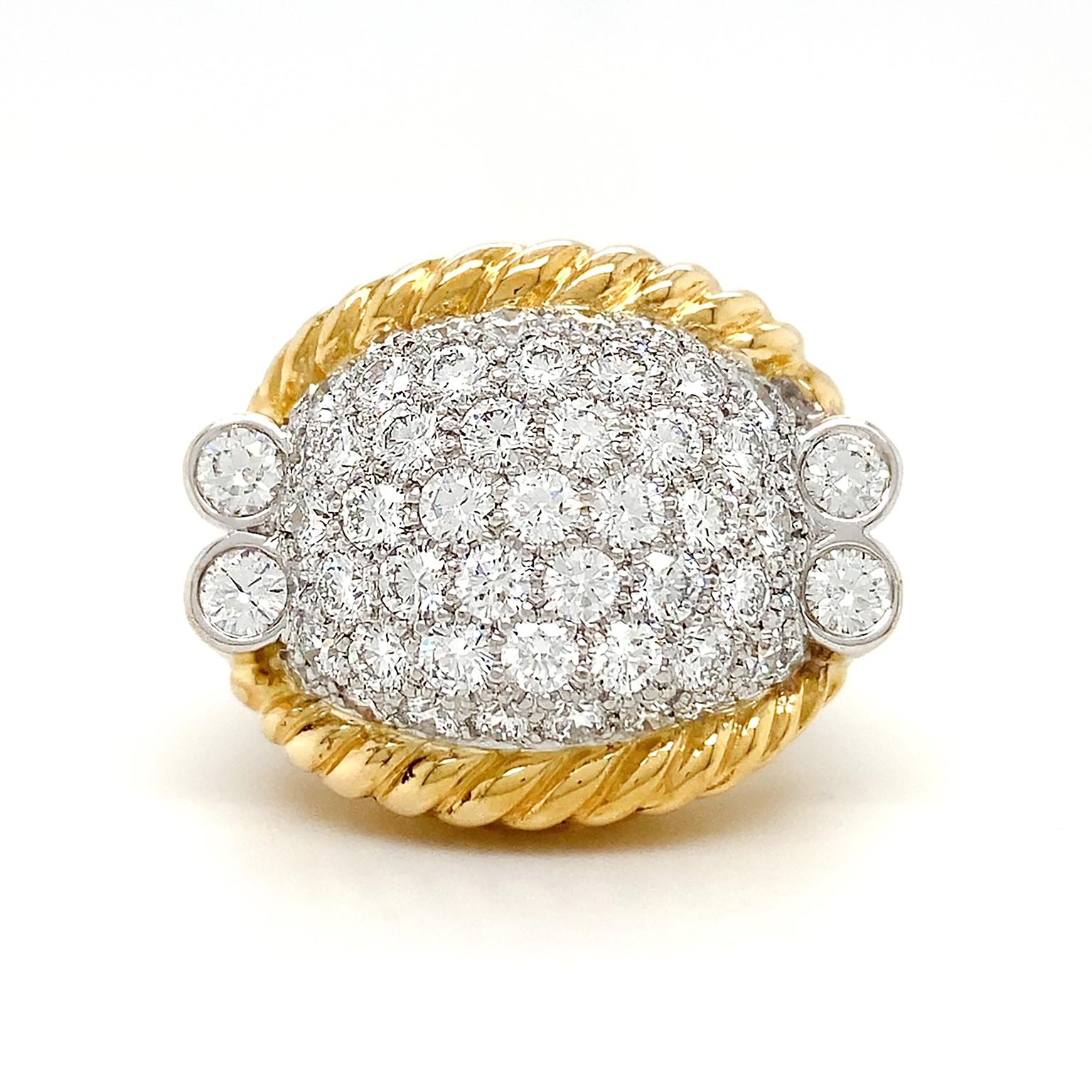 The crest of this ring is a luminance of white light. A raised oval of platinum is encrusted with a collection of brilliant cut diamonds. Along the sides are a trio of stacked 18k yellow gold ropes. A double band with platinum set diamond tips