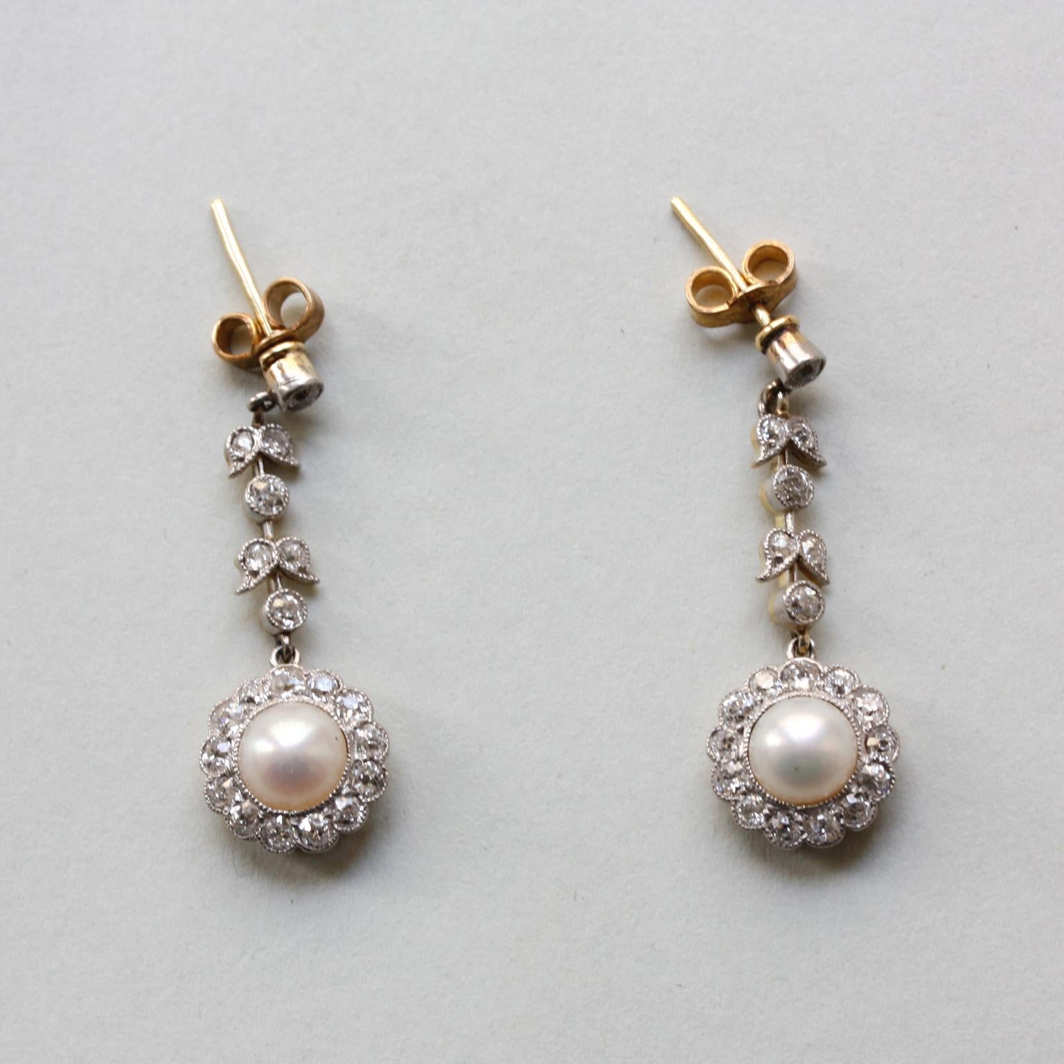 A pair of Edwardian gold earrings with a platinum mille griffe set white bouton pearl and a cluster of 13 old-cut diamonds around it, hanging from a guirlande with leaves also with old-cut diamonds. England, circa 1915.

Weight: 4.00