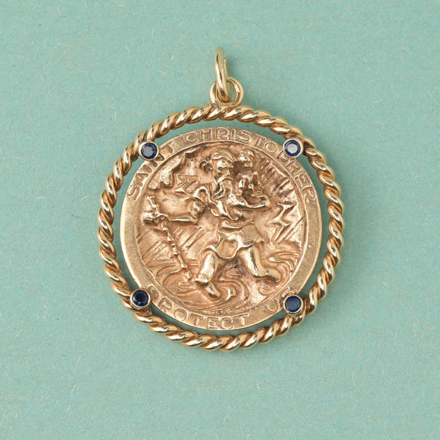 A large 14 carat gold pendant with Saint Christopher and the text: ‘Saint Christopher Protect Us’, decorated with a border of twisted gold rope and four round sapphires, American, circa 1970.

weight: 25.35 gram
dimensions: 5 x 3.8 cm