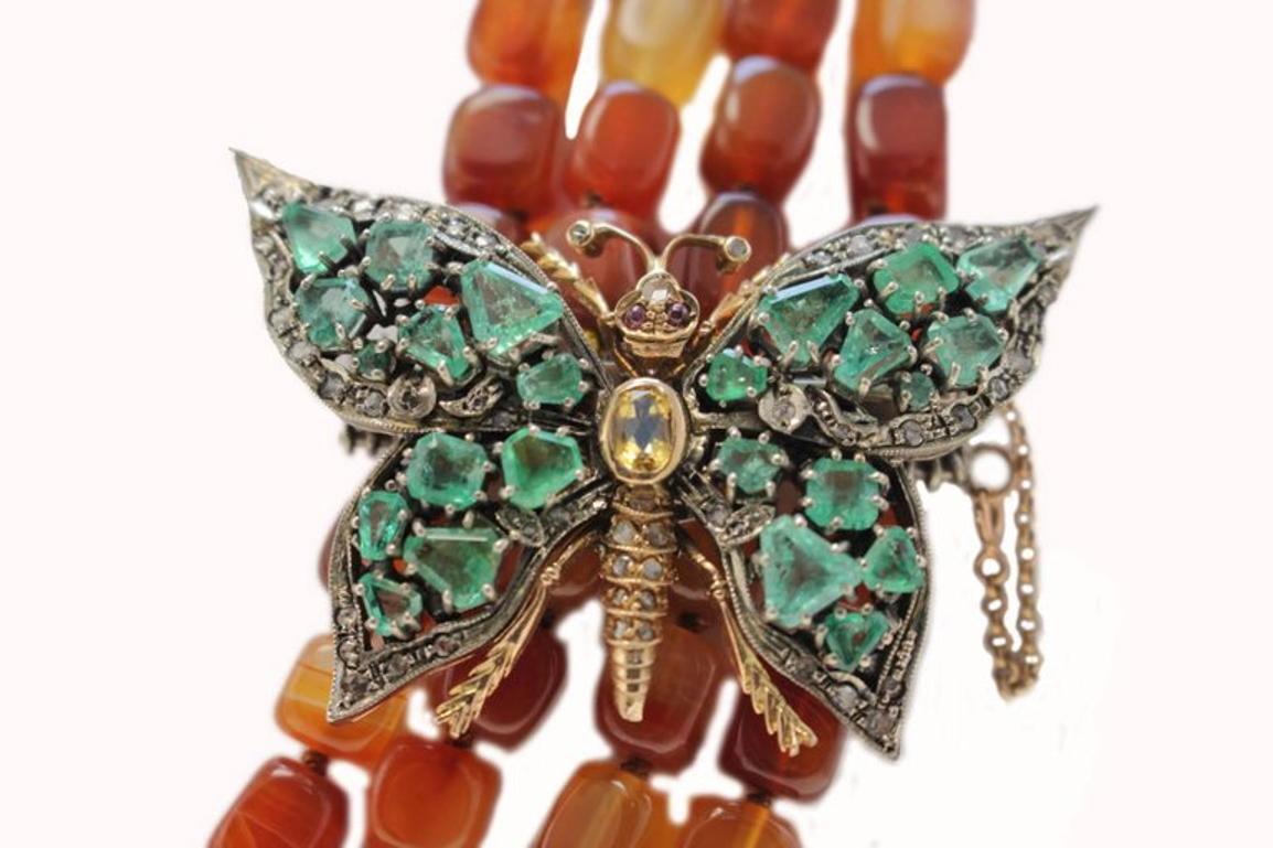 Enchanting carnelian multi strands necklace, embellished with a clasp of a butterfly shape, with emeralds as wings, garnets as eyes, in the middle of the body a single topaz and all around shiny diamonds. The clasp is mounted in 9 Kt rose gold and