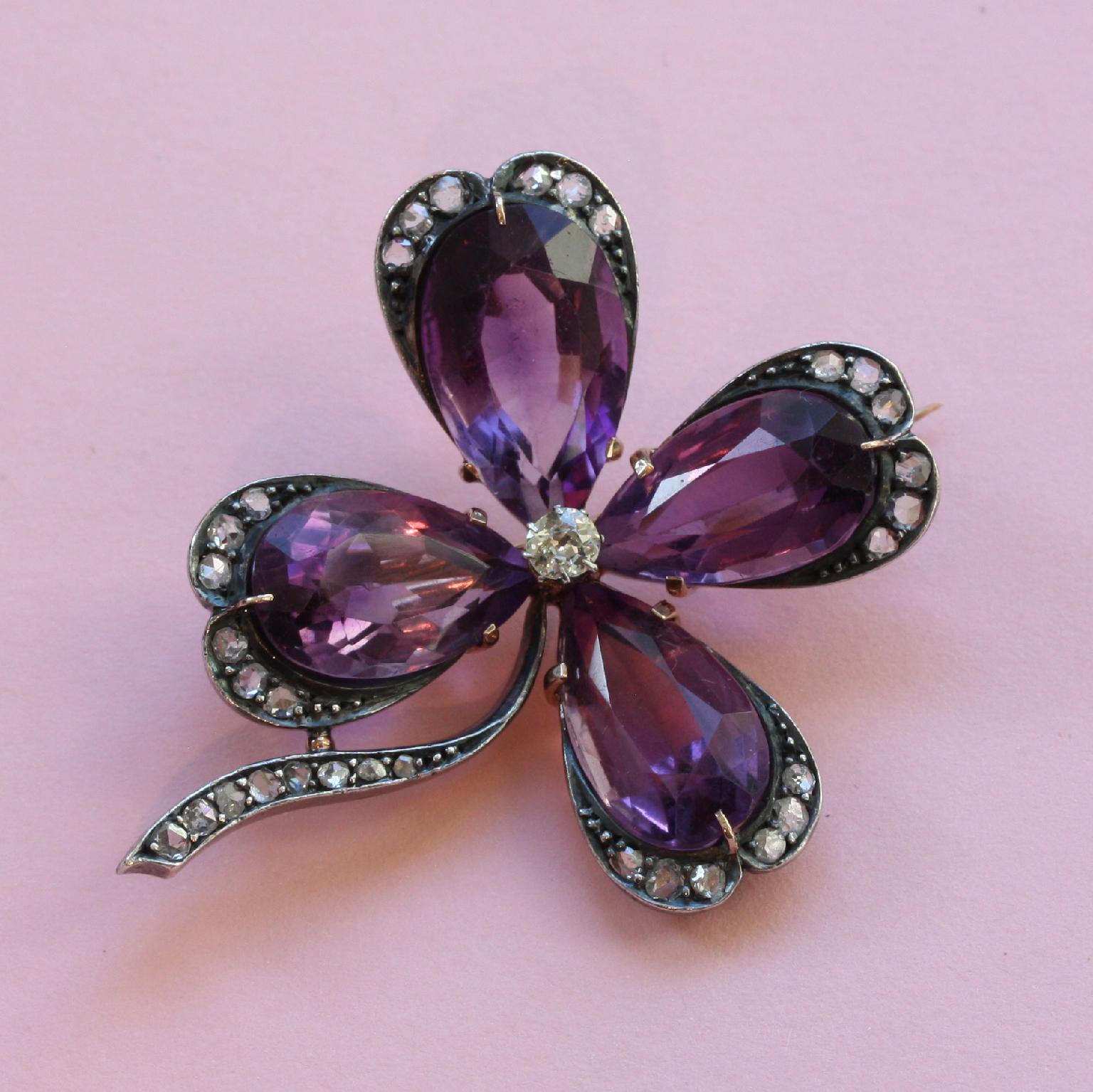 A large gold clover four brooch in gold with four large pear shaped amethysts in different sizes, the end of each petal has a border or rose cut diamonds, as has the stem, the heart of the clover is set with an old cut diamond, circa 1900.

weight:
