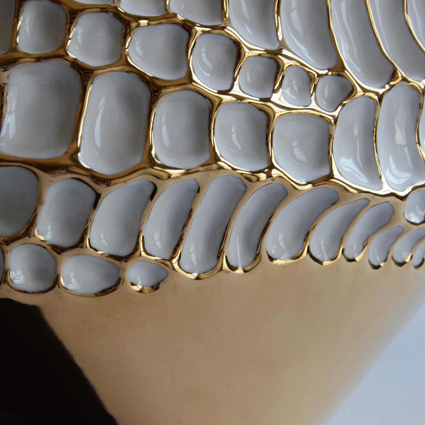 The particular elliptical shape and textured surface resembling hammering, are the result of a meticulous study on the microscopic magnification of a seed. This precious vase in glazed porcelain is decorated with gold 23-karat, applied by expert