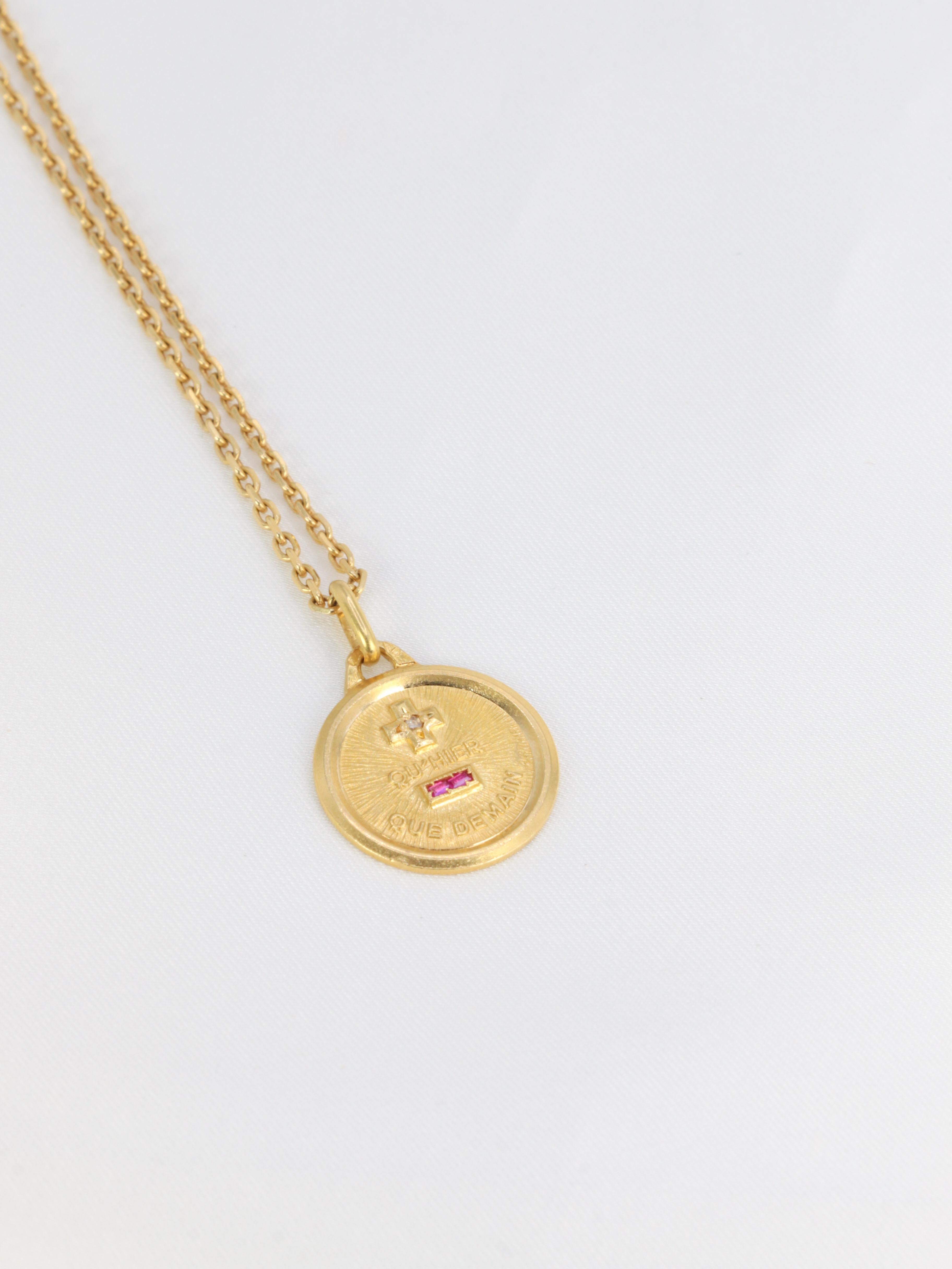 18Kt (750°/°°) yellow gold Love medal set with baguette-cut synthetic rubies and a small rose-cut diamond.
The famous phrase Plus qu'hier Moins que demain, inspired by two verses by Rosemonde Gérard Rostand, is written on the medal.
French work from