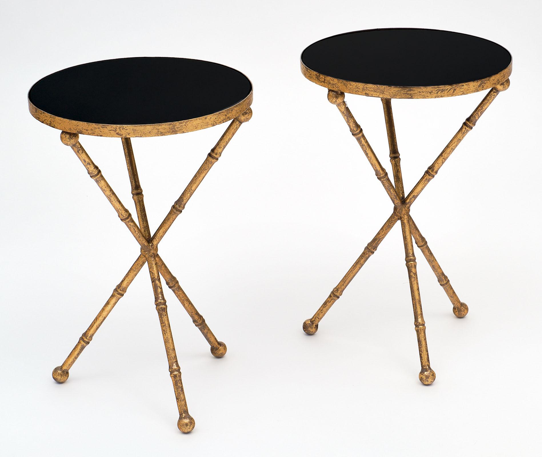 Pair of round gold leaf tripod side tables with stylized bamboo base and black glass top. This is a beautiful and dynamic set with lots of character!