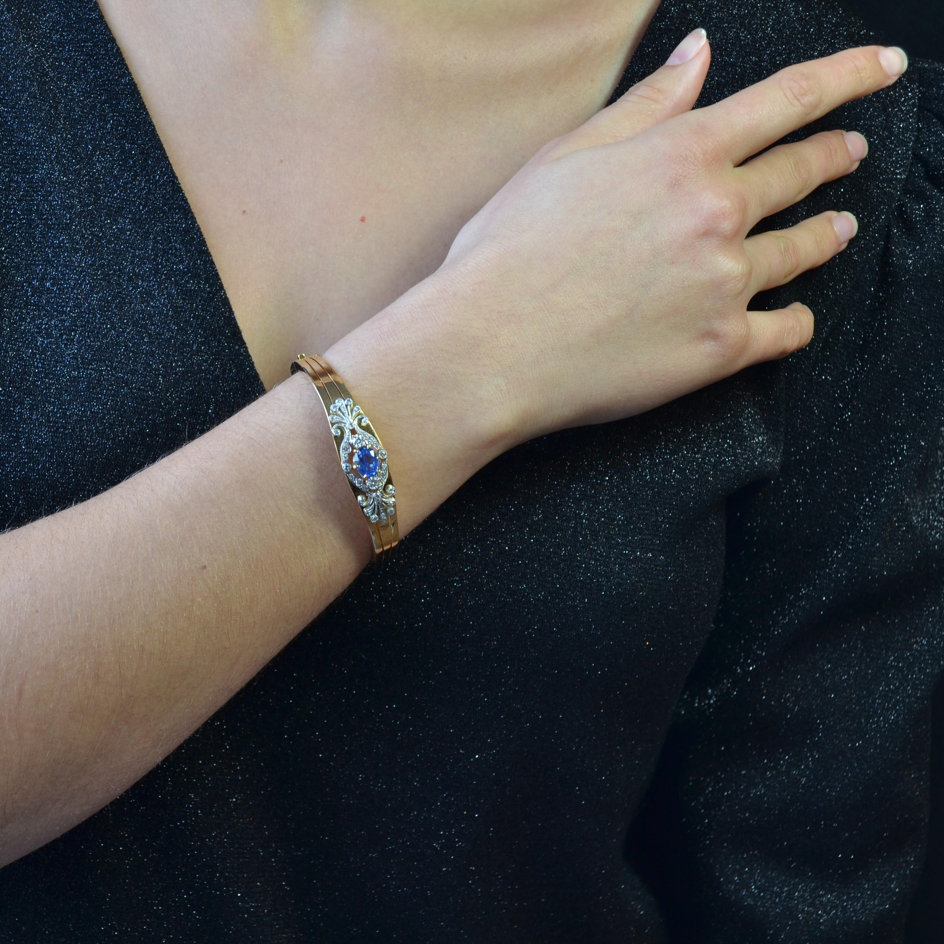 Bracelet in 18 carat yellow gold, eagle head hallmark.
An oval opening bangle type bracelet with 3 flat golden bands at the front and an openwork floral design set with diamonds and a central blue sapphire. The clasp is a ratchet with safety chain.