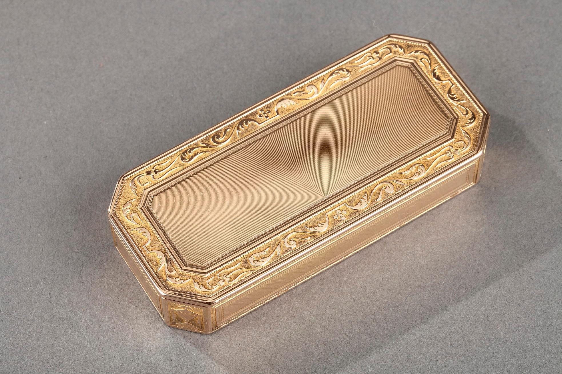 Rechteckige Goldbox mit geschnittenen Seiten. Der scharniergelagerte Golddeckel ist mit konzentrischen Linien verziert, die von einem floralen Fries aus Blattwerk auf Amati-Goldgrund eingerahmt sind. Der Rahmen besteht aus vier Paneelen, die mit