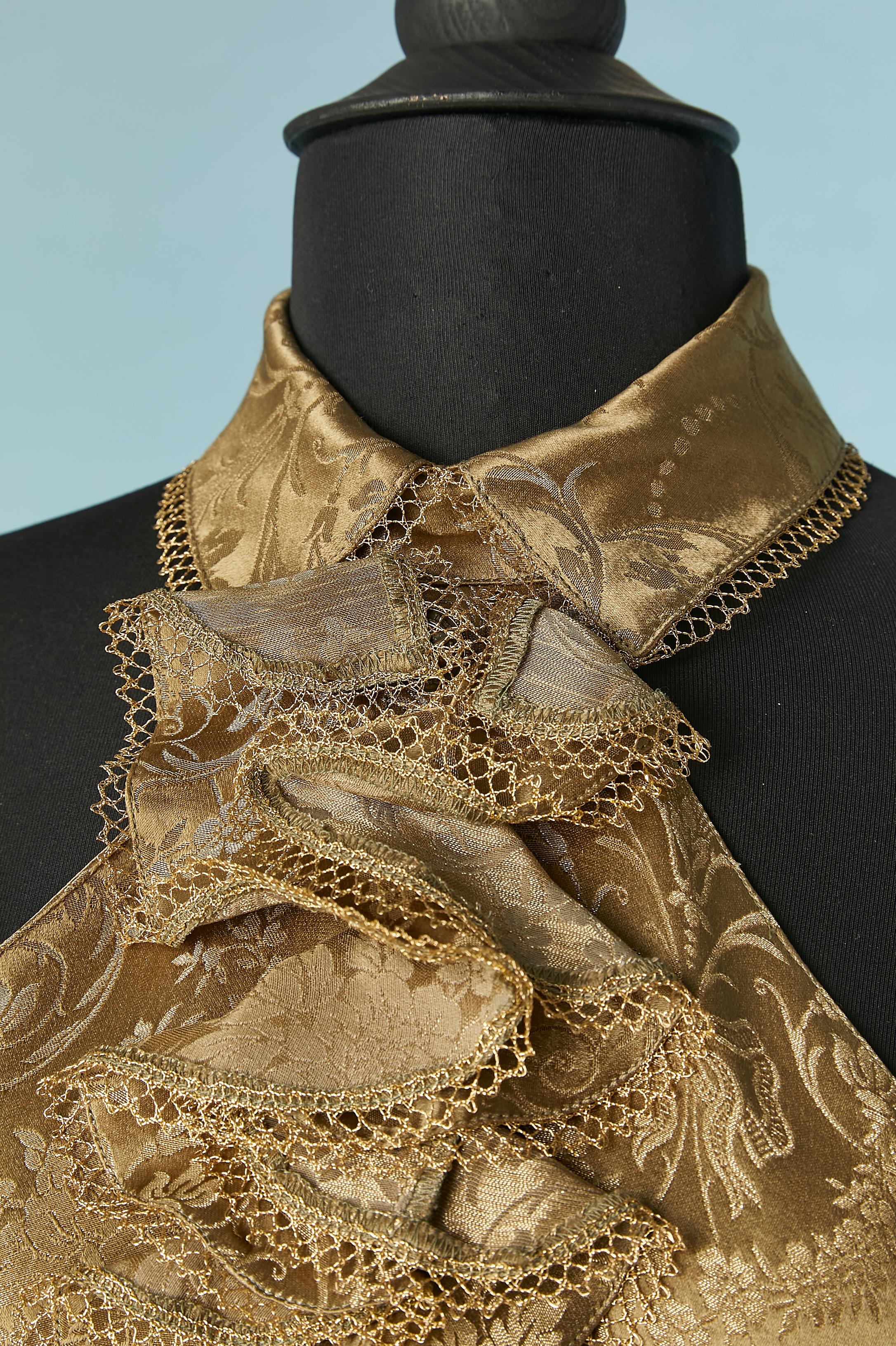 Gold brocade backless top with ruffles jabot on the front . Fabric composition: 54% rayon, 32% silk, 14% polyester. 
Decorative buttons on the middle front and one button closure on the top middle back. Belt to tie on the middle back. Gold lurex
