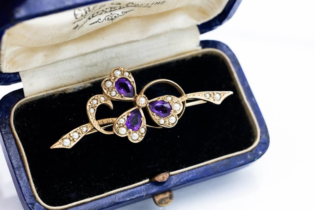 Un'affascinante spilla in oro 9 carati (finezza 0,375) a forma di trifoglio. Una delicata spilla decorativa decorata con tre ametiste e piccole perle.

Una scelta perfetta per chi apprezza i gioielli classici senza tempo.

Ottime condizioni, nessun