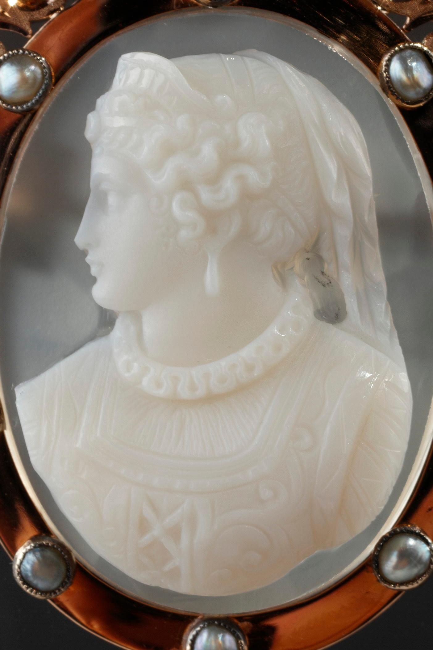 Cameo on brown agate featuring a young woman looking toward the left. The artist intricately sculpted the white vein of the agate to bring the delicate profile to life. The young woman is wearing a dress from the 17th century with a laced bodice and