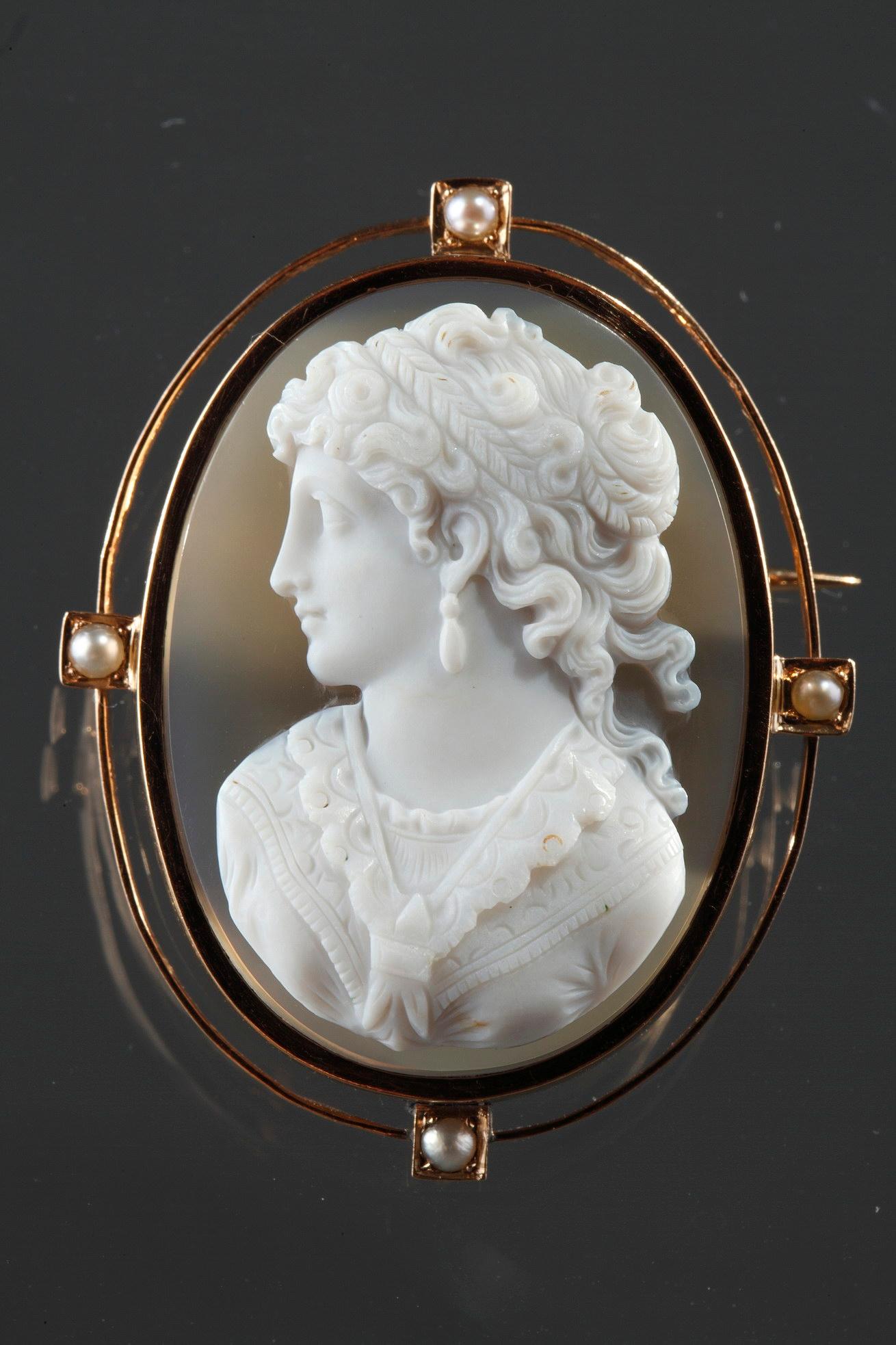 Cameo on blue-gray agate featuring a young woman looking toward the left. The artist intricately sculpted the white vein of the agate to bring the delicate profile to life. The young woman is wearing a dress with lace scarf.

His hair is knotted and