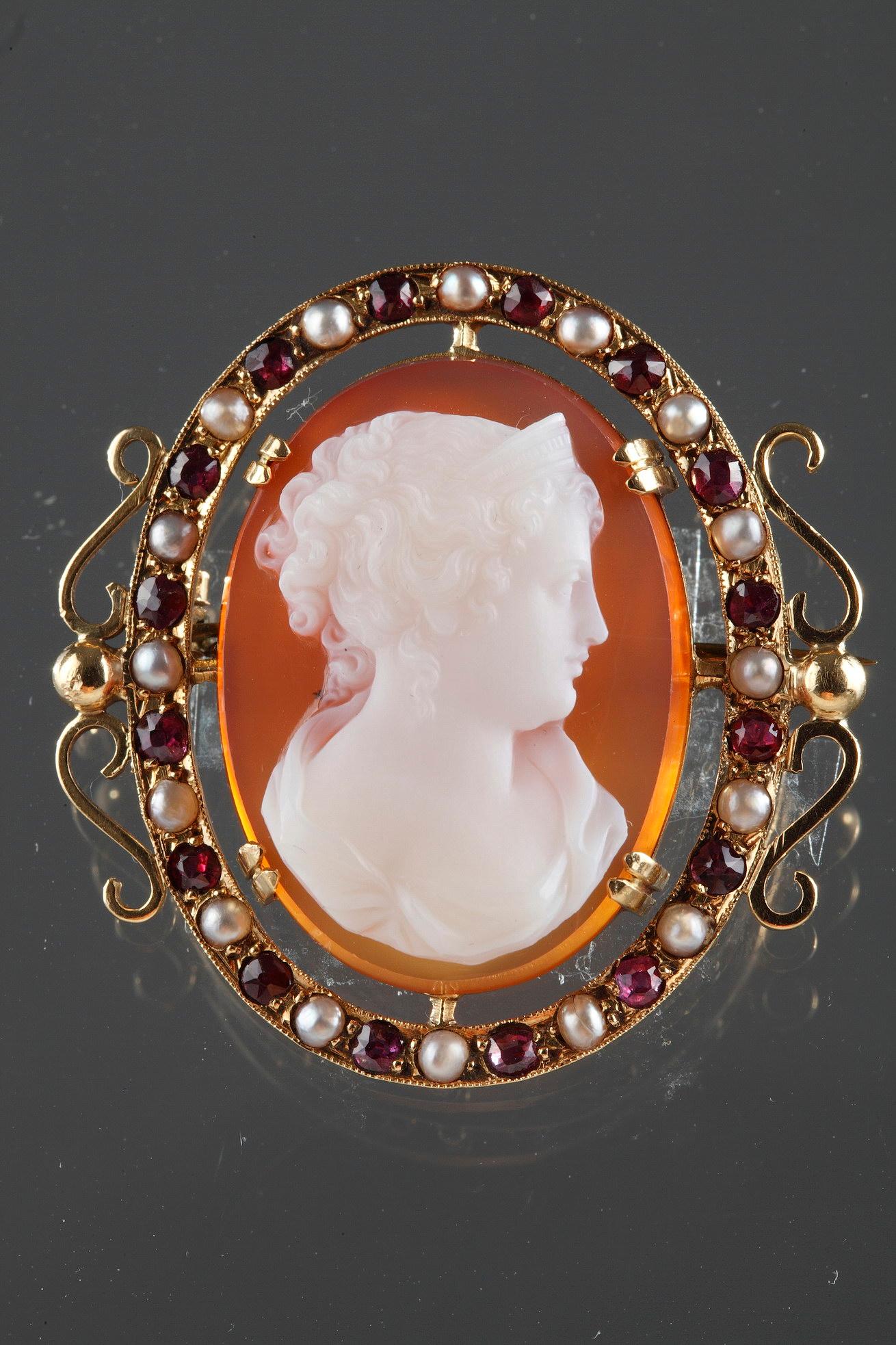 Cameo on pink agate featuring a young woman looking toward the wright. The artist intricately sculpted the white vein of the agate to bring the delicate profile to life. The young woman is wearing an antique dress This woman has her hair pulled back