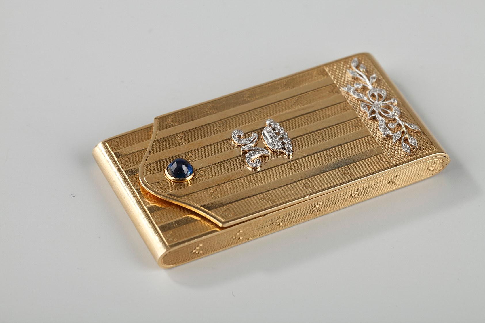 Intricately decorated rectangular gold case. The case opens in the front like a small purse. The entirety of the case is embellished with intricate geometric patterns of parallel stripes alternating with bands of polished gold. The upper part of the