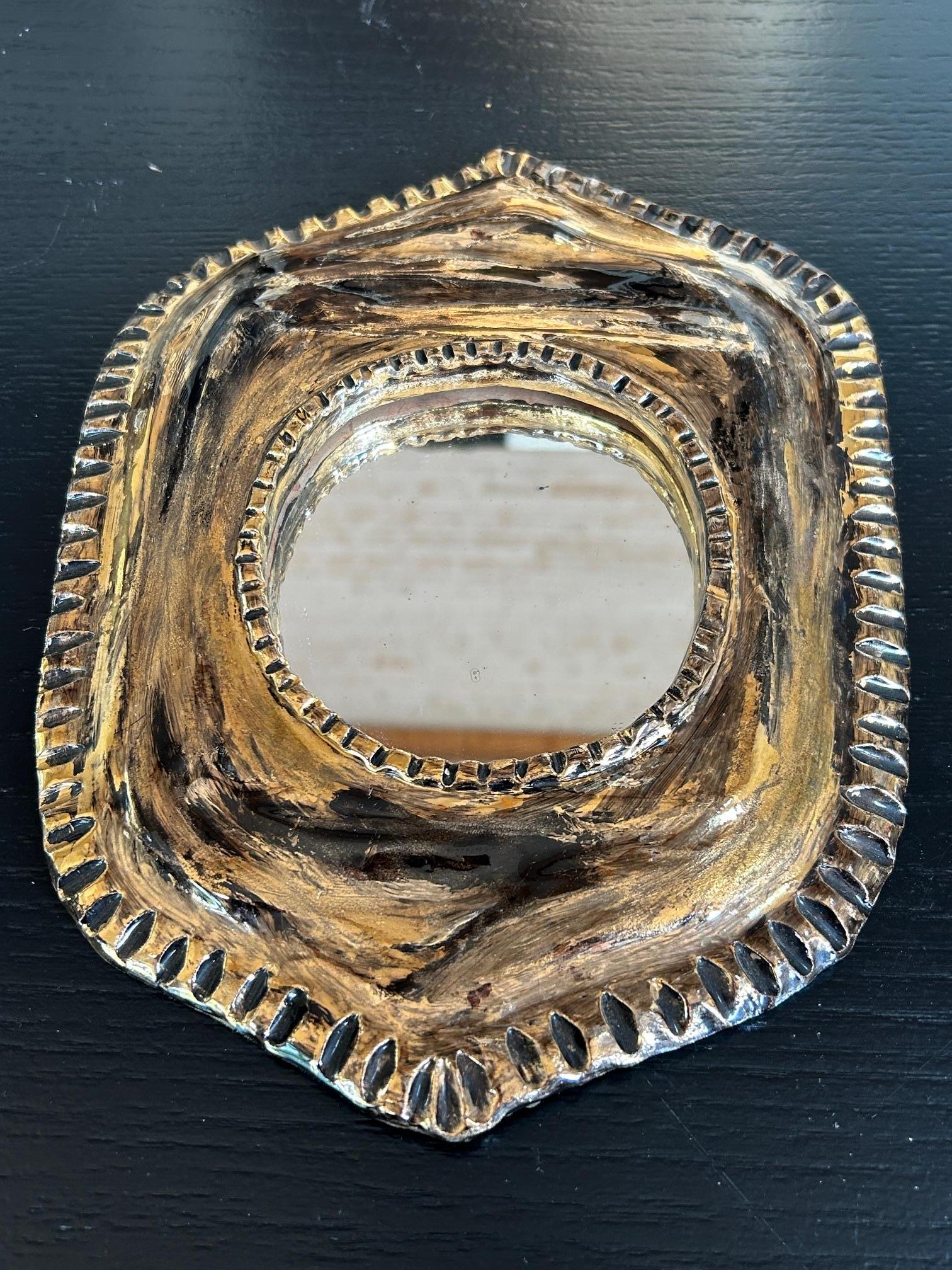 Magnifique miroir mural des années 1960, réalisé en céramique émaillée avec d'élégants détails en relief rappelant le style raffiné de Mithé Eleg. La bordure présente un design structuré et délicatement texturé, rehaussé par un émail doré lumineux