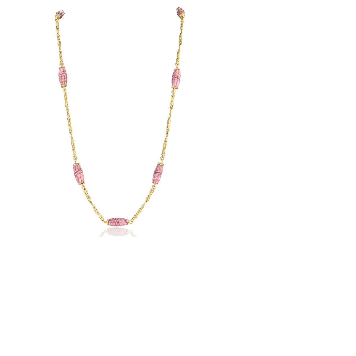 An 18 karat gold chain with 7 ribbed barrel-shaped rhodochrosite beads. The dynamic links of the chain feature an alternating pattern of elongated, polished metal design elements with shorter, textured sub-links cast so as to mimic the appearance of