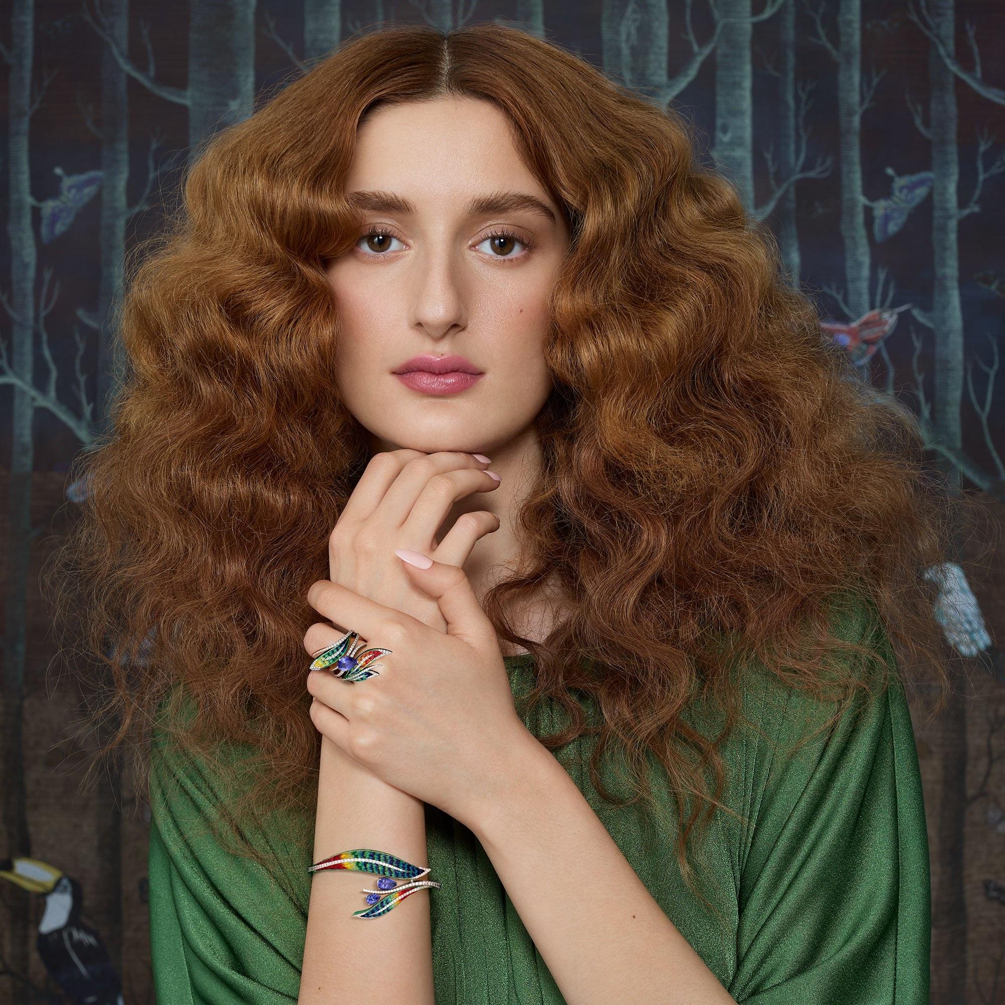Behold the Quetzal ring, a tropical masterpiece that captures the spirit of lush paradise. 
Two gracefully intertwined leaves guide your gaze to the center, where there lies a splendid tanzanite. Vibrant green, yellow, and red micromosaics fill the