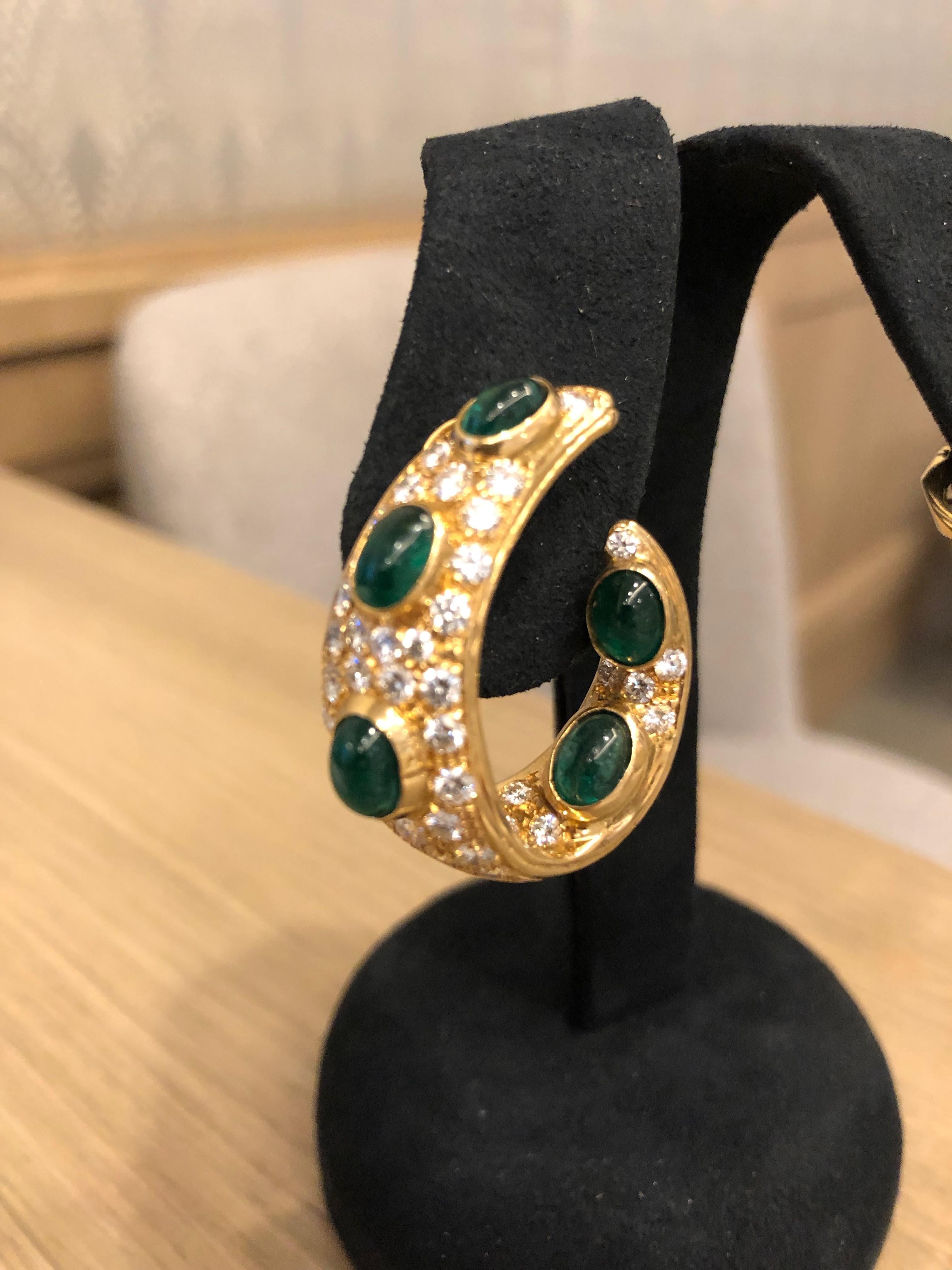 A pair of British Early 21st-Century 18 karat gold earrings with diamonds and emeralds by Graff. The compressed gold hoops feature 10 cabochon emeralds with an approximate total weight of 5.8 carats and are studded with an additional 78 VS clarity,