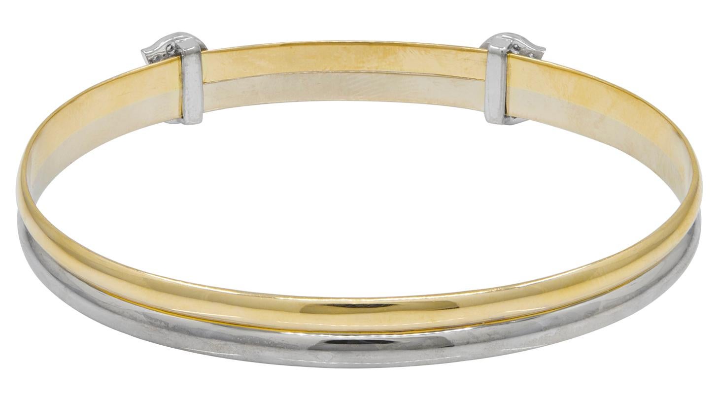 Classic and elegant slim cuff bracelet.  Made, signed and numbered by CARTIER.  18K yellow and white gold, with diamond-encrusted CC logo.  On oval slip-on that 