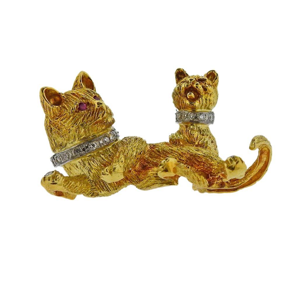 Whimsical 18k yellow gold brooch, depicting a cat and kitten, adorned with ruby eyes and approx. 0.14ctw in diamonds. Brooch is 36mm x 26mm. Weight is 15.9 grams. 