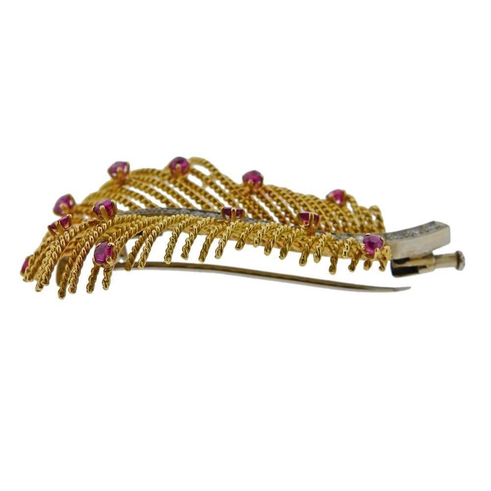 18k yellow gold feather brooch, set with rubies and approx. 0.08ctw in diamonds. Brooch is 56mm x 32mm. Marked 750 and with gold mark. Weighs 12.7 grams.
