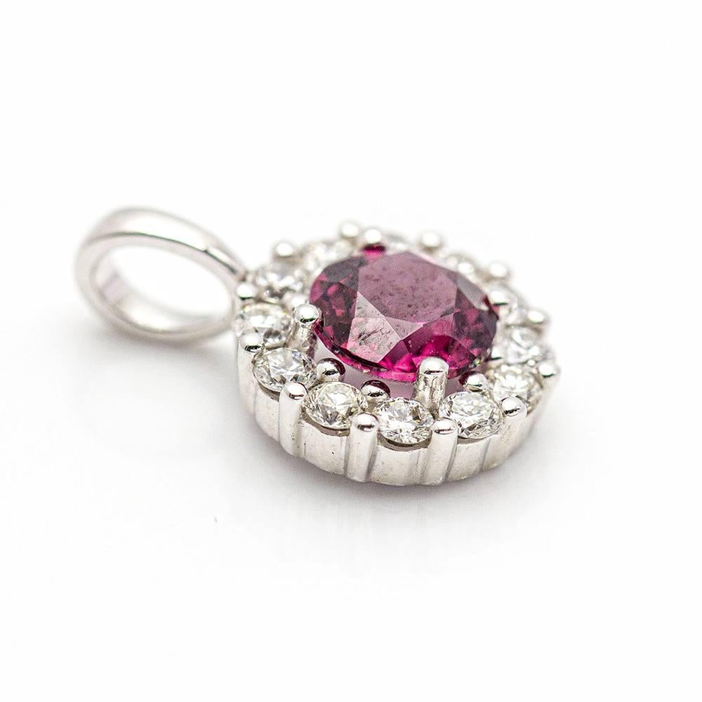 Gold Pendant for woman : 12x Brilliant Cut Diamonds with a total weight of 0,22 cts. in G/VS quality : 1x Rhodolite (Brazilian Garnet in purple red colour) of 0,30ct. : 18 kt. White Gold : 0,90 grams : 1,3 cm length (including ring) : Brand new