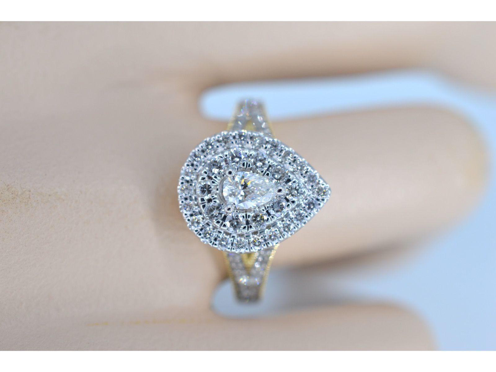 This gold drop-shaped entourage ring is a truly stunning piece of jewelry that features a combination of brilliant cut diamonds and a pear-shaped diamond. The drop-shaped design adds a unique and elegant touch to the ring, while the brilliant cut