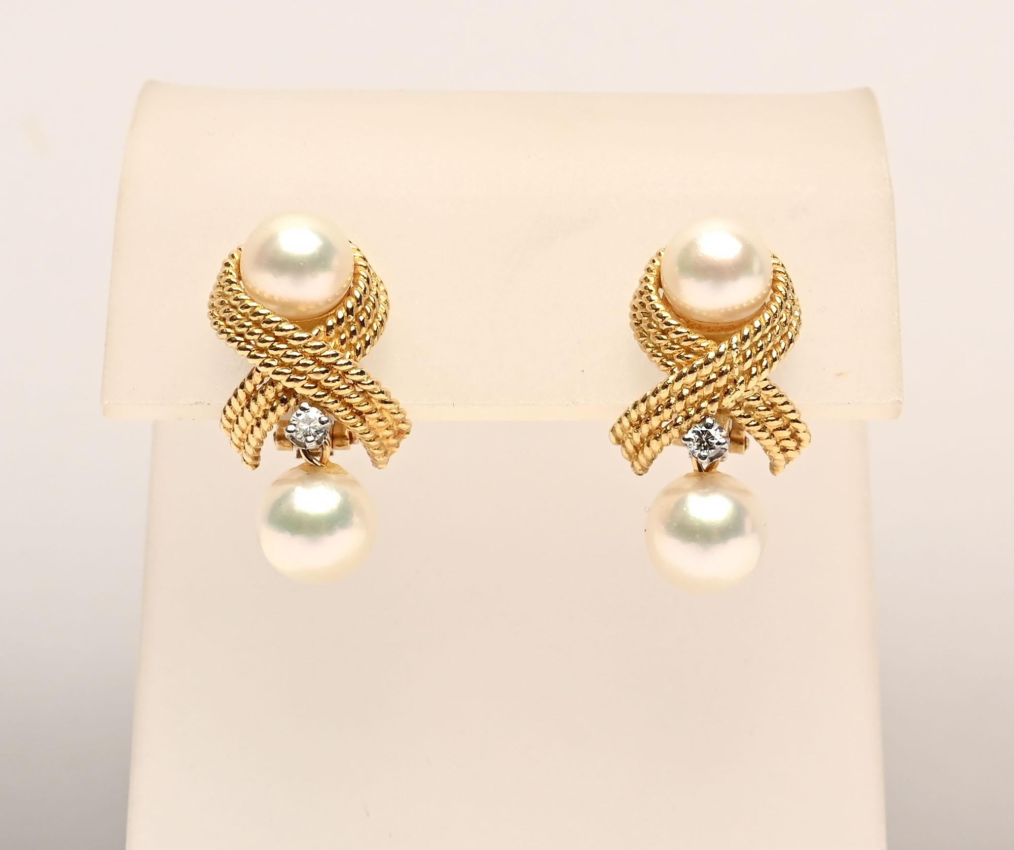 Criss cross 18 karat gold earrings with an 8 mm pearl on top and below. The bottom pearl hangs from a tiny loop with a diamond that is approximately .2 carats. The diamonds are G color; VS quality. The gold criss cross consists of three bands of