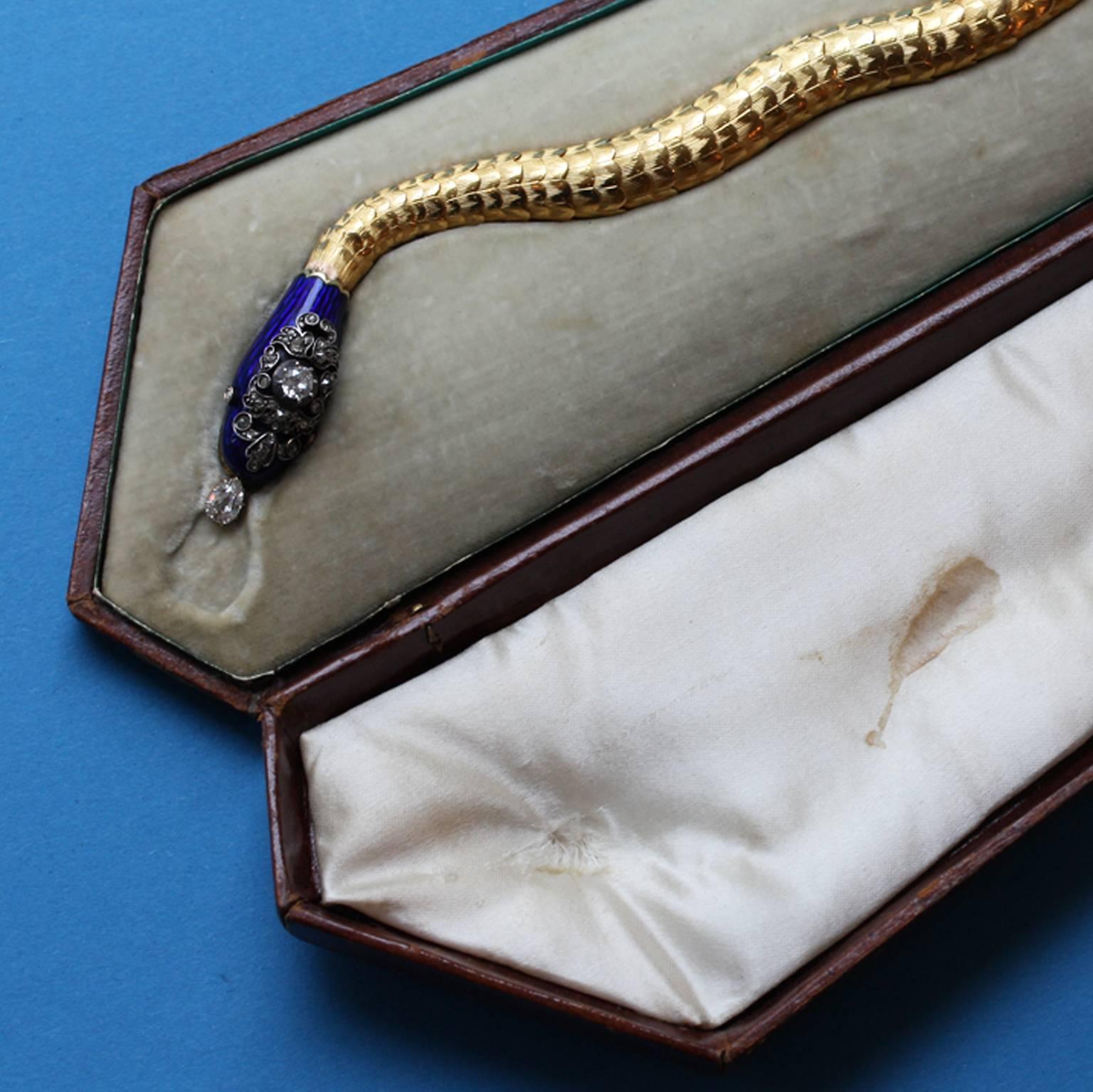 A gold snake bracelet with an enamel and diamond head, a – later replaced – pear shaped diamond suspends from its jaws, with a concealed clasp and in its original coffin shaped case, England, circa 1840.

weight: 38 grams

Illustrated in