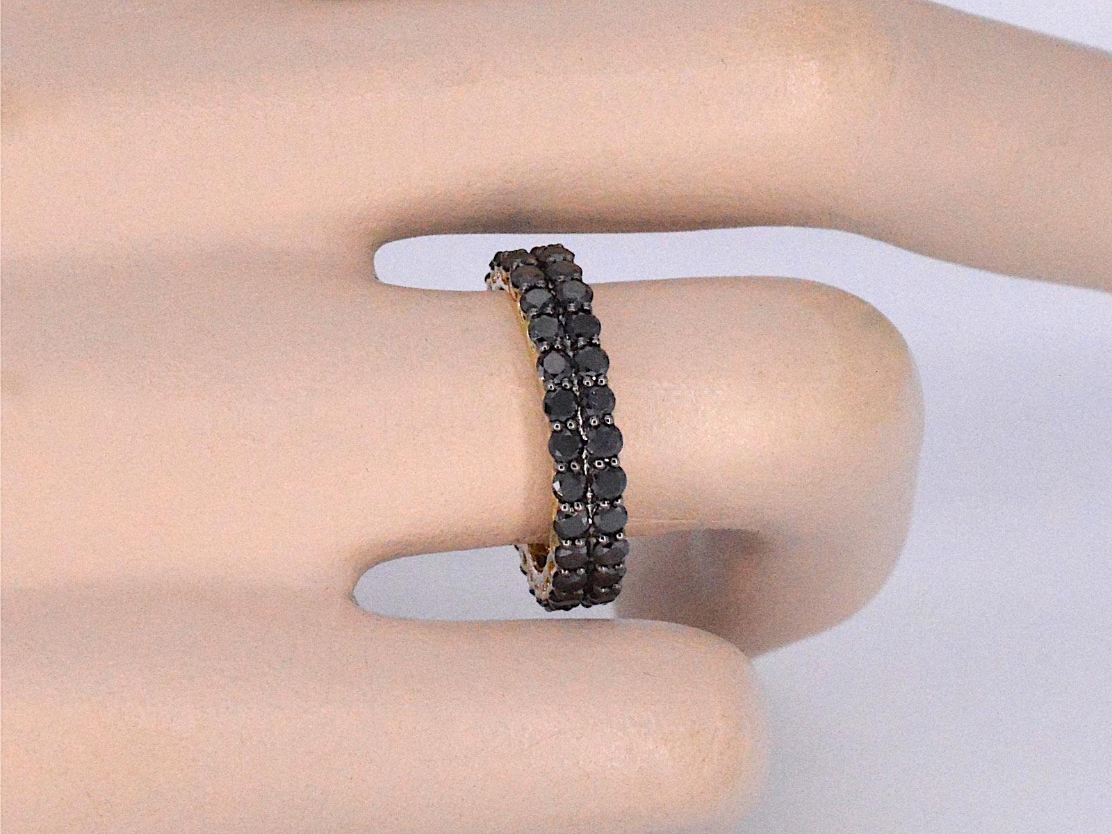 This gold eternity ring is a sleek and stylish piece of jewelry, featuring a band of black diamonds that wrap all the way around the ring. The gold is a high-quality metal that is known for its durability and lustrous properties. The black diamonds