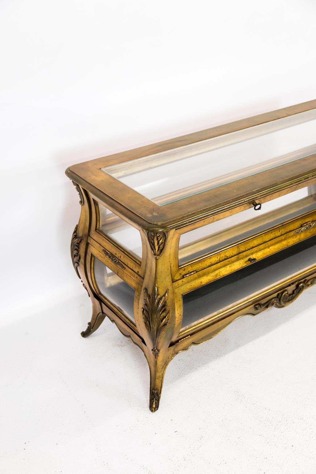Gold four sided Bombe vitrine, has a double compartment. Long doors fold down to expose an upper glass shelf and black velvet on the lower shelf. The cabriole legs have carved acanthus leaves on all four sides.