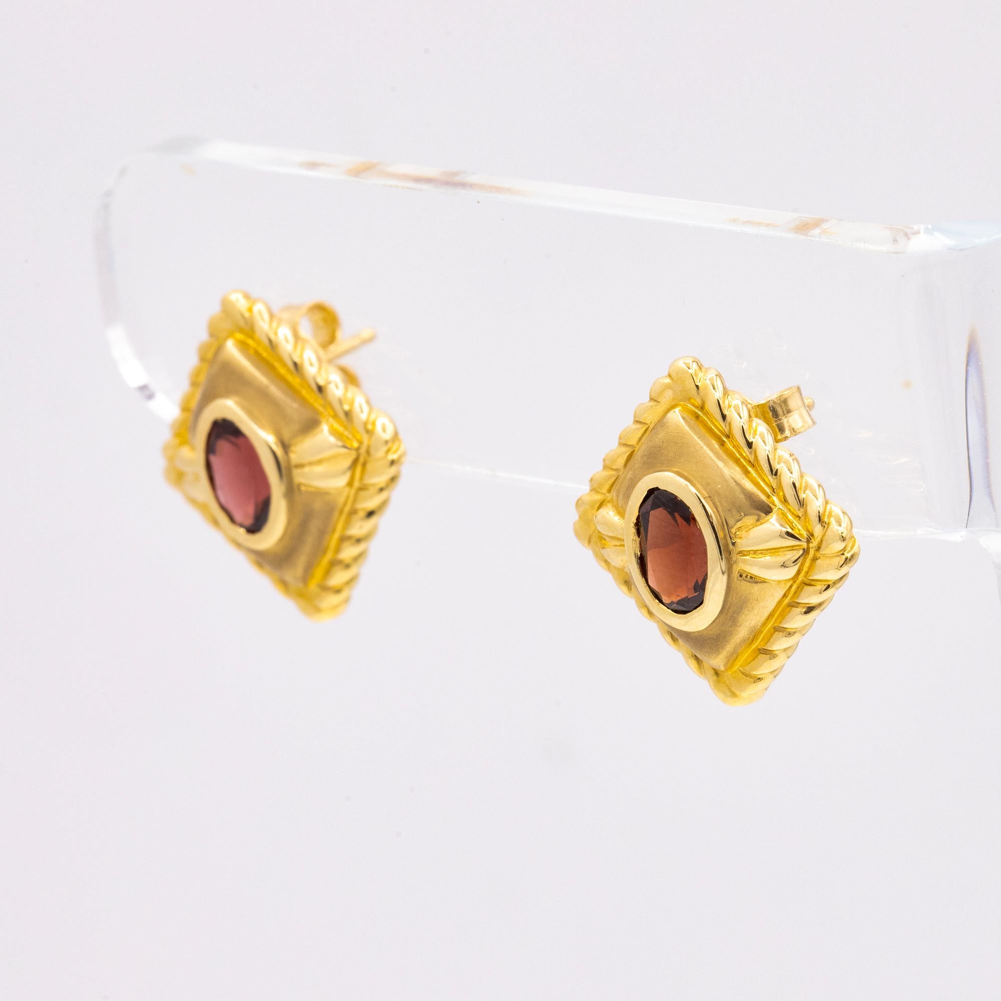 Vintage Earrings set in 14kt Yellow Gold. Bezel set design holding two expertly cut Oval shaped Garnets. These studs have a simple squared style with a beaded edging design. 