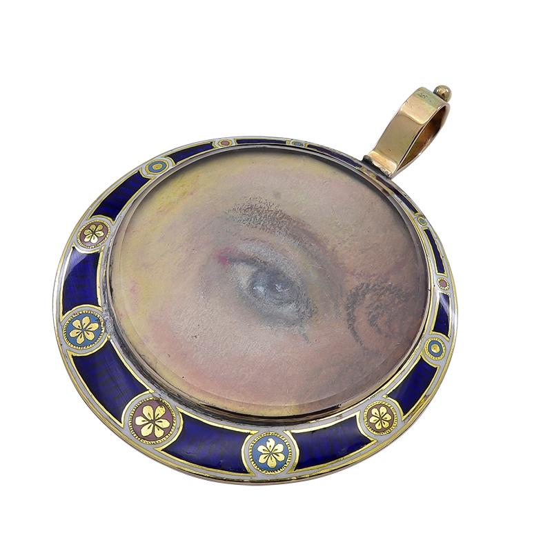 A superb example of the rare and romantic Georgian Lover's Eye jewelry:  a pendant with a very fine hand-painted eye.  The portrait shows a well-detailed eye, with a tendril of hair at the temple.  Set in an 18K gold and enamel mounting.  1 1/3